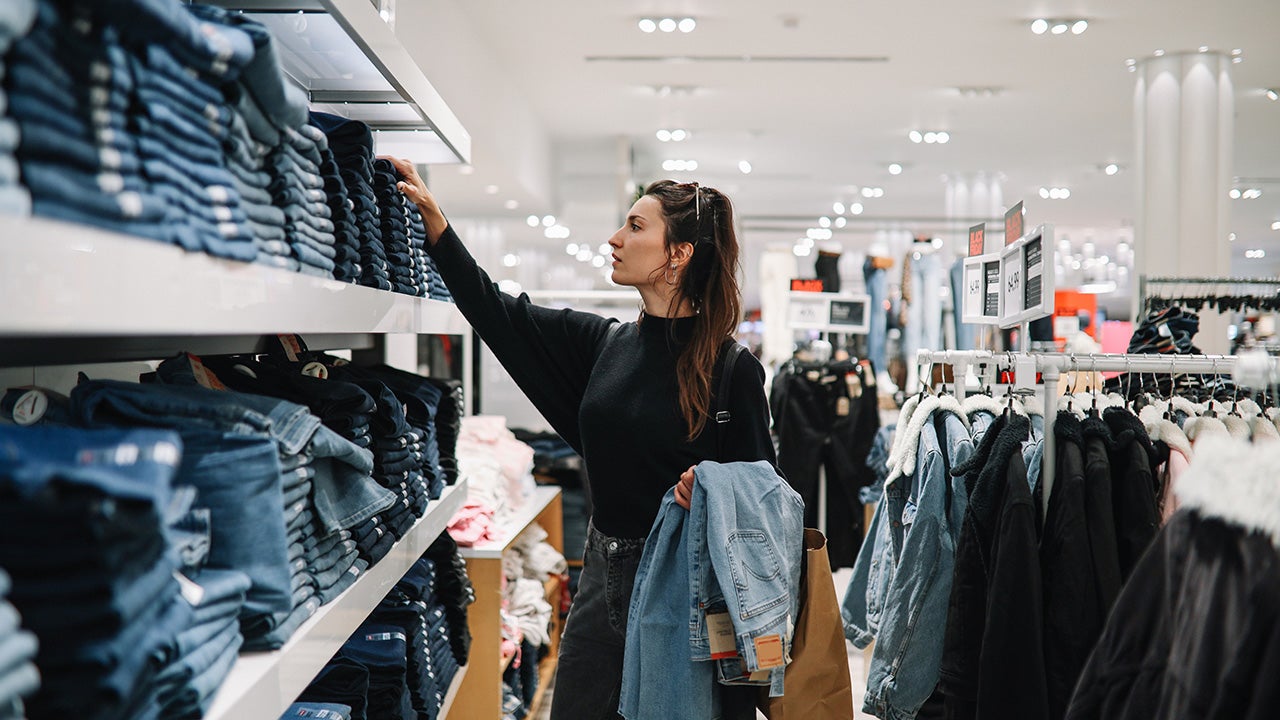 Woman in mid 30s goes shopping for denim jeans in a clothing store.