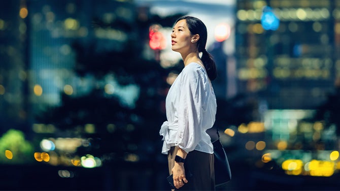 Person in white top stands in city at night with blurred lights.