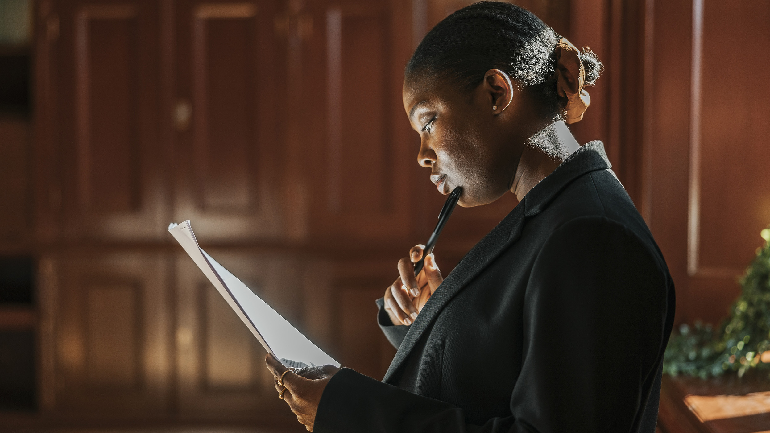 Person reading a document and holding a pen in a wood-paneled room