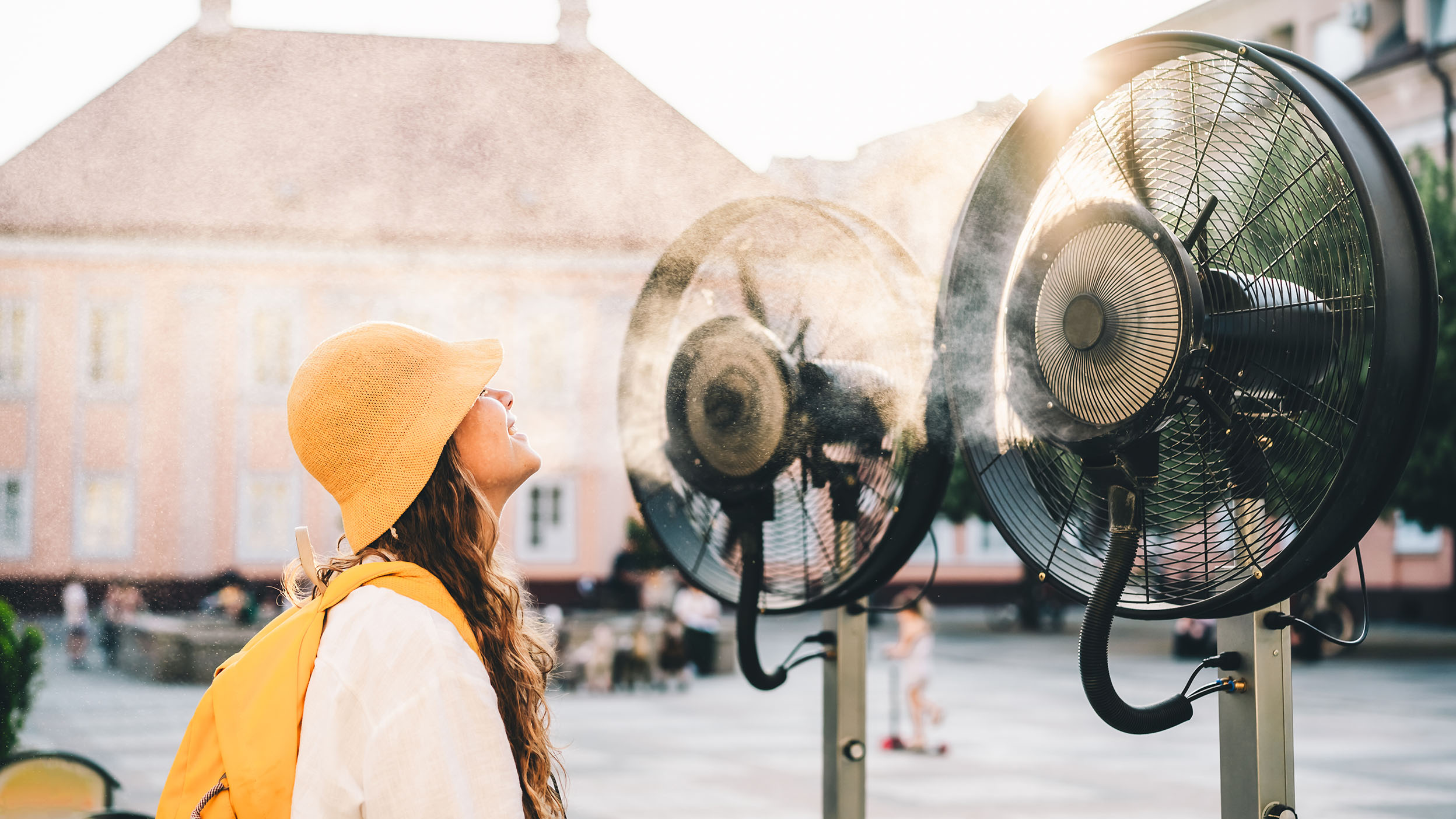 Person cooling off beside outdoor misting fans on a hot day