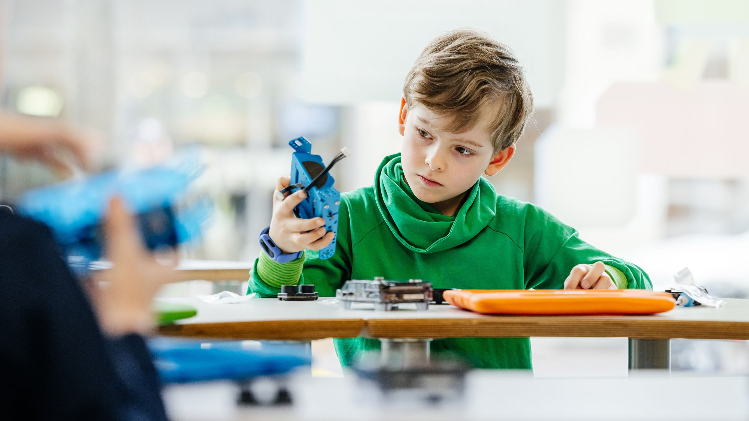 Person examining a blue electronic device at a table with tools and components.