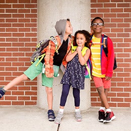 Children%20with%20backpacks%20standing%20together%20outside%20a%20school%20in%20front%20of%20a%20brick%20wall.