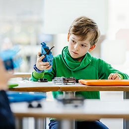 Person%20examining%20a%20blue%20electronic%20device%20at%20a%20table%20with%20tools%20and%20components.