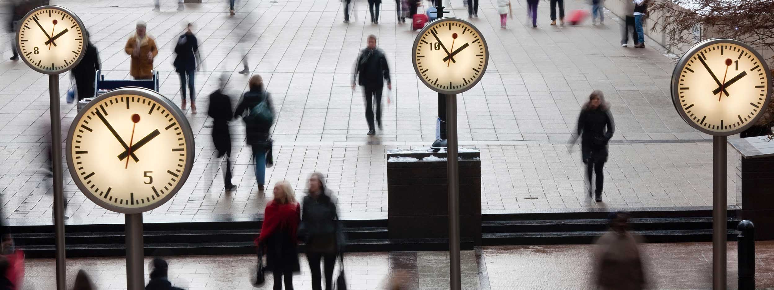 Busy street scene with blurred pedestrians and multiple clocks showing different times.