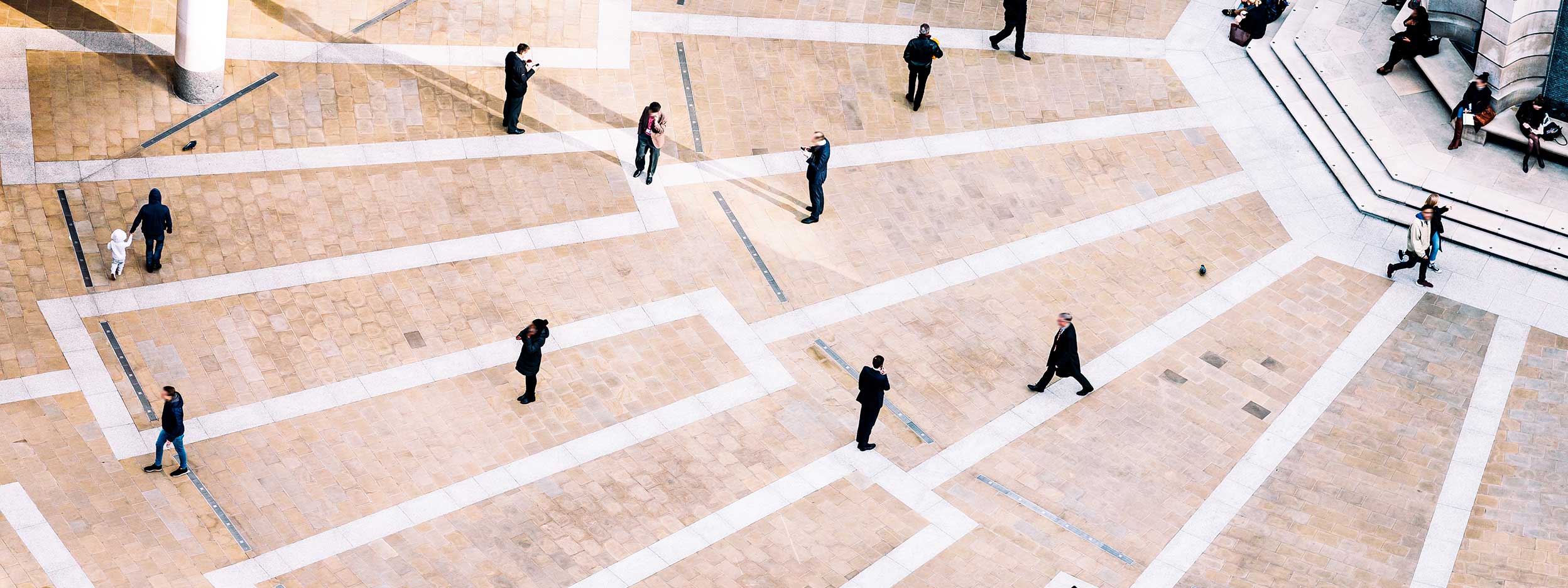 People walking across a large urban plaza with geometric paving