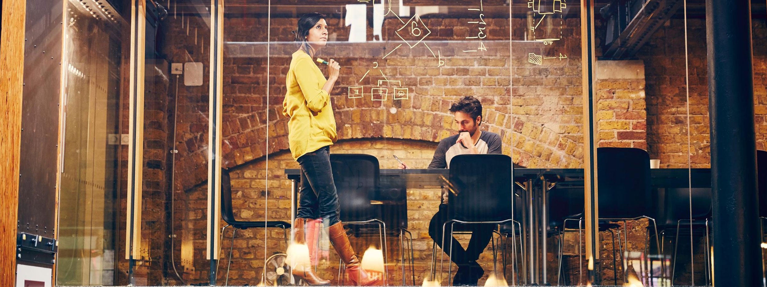 Two people seated at a table inside a glass-enclosed room, engaged in conversation.