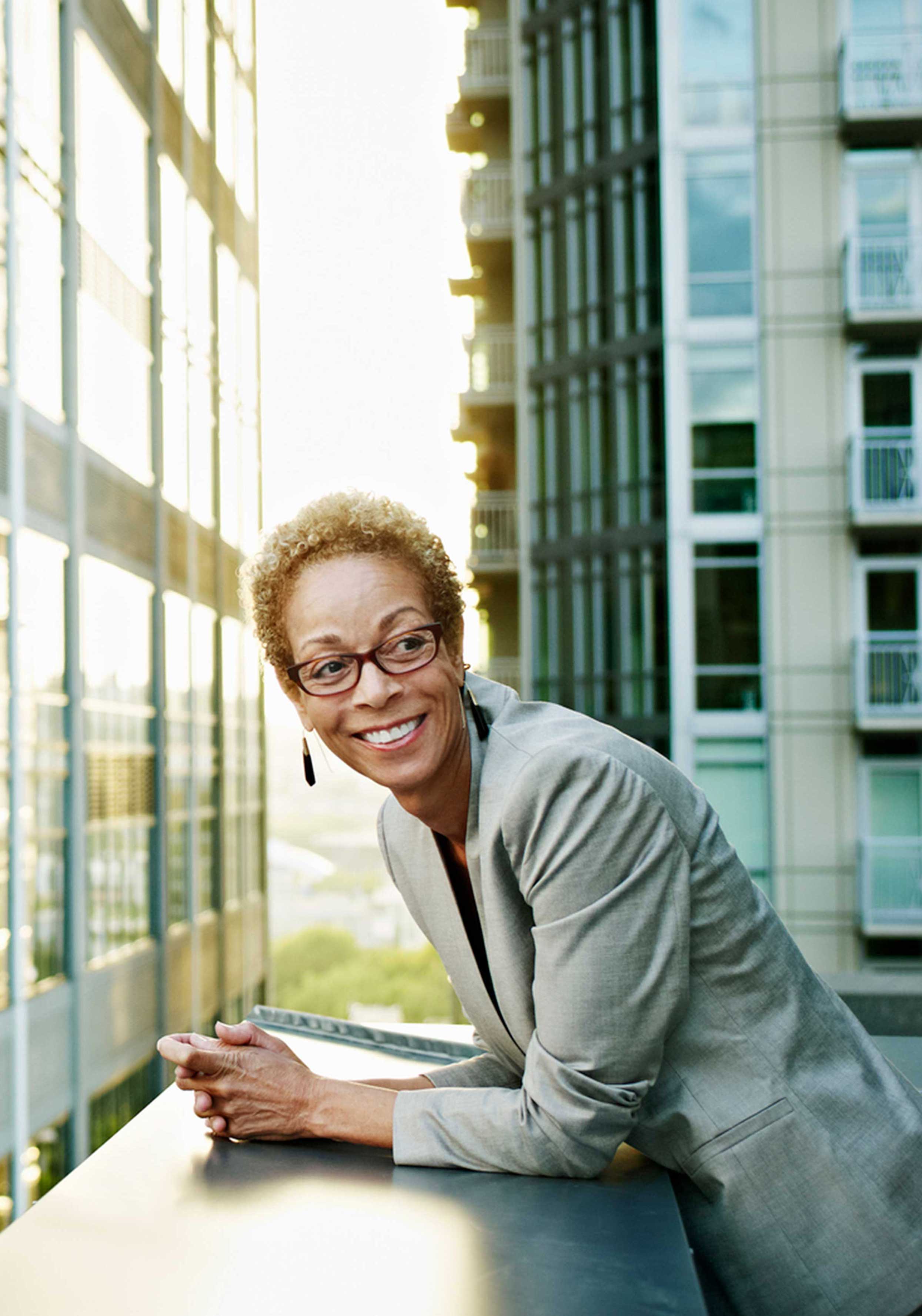 A person leaning on a balcony railing between tall modern buildings