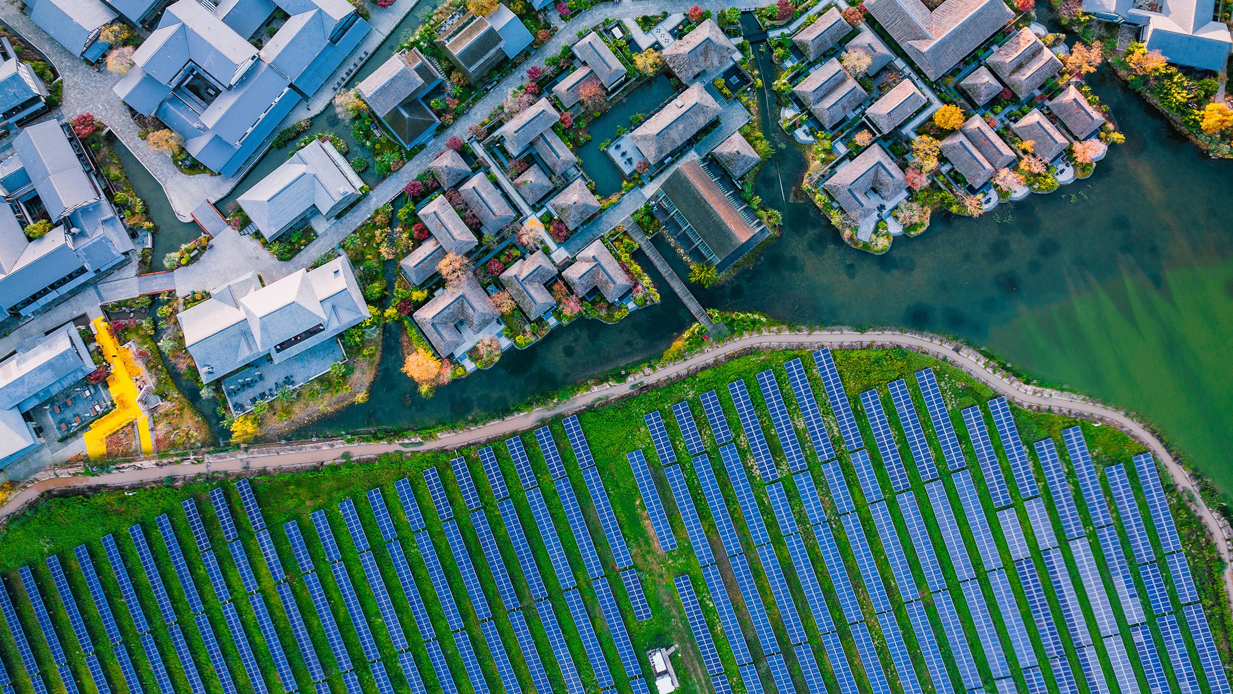 A bird's eye view of a residential area showcasing houses surrounded by greenery, and an area of solar panels. Displaying environmental sustainability.