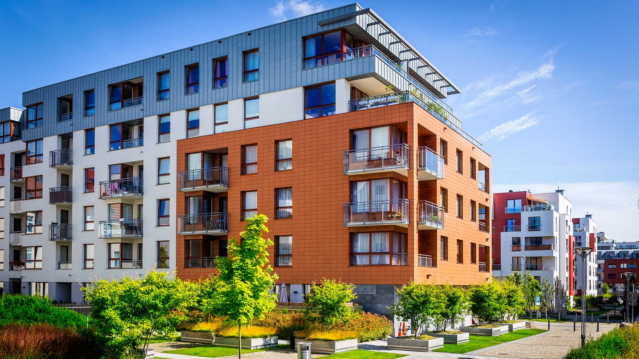 Blick auf ein modernes Haus mit einer teilweise orangefarbenen Fassade. Weitere Häuser im Hintergrund.