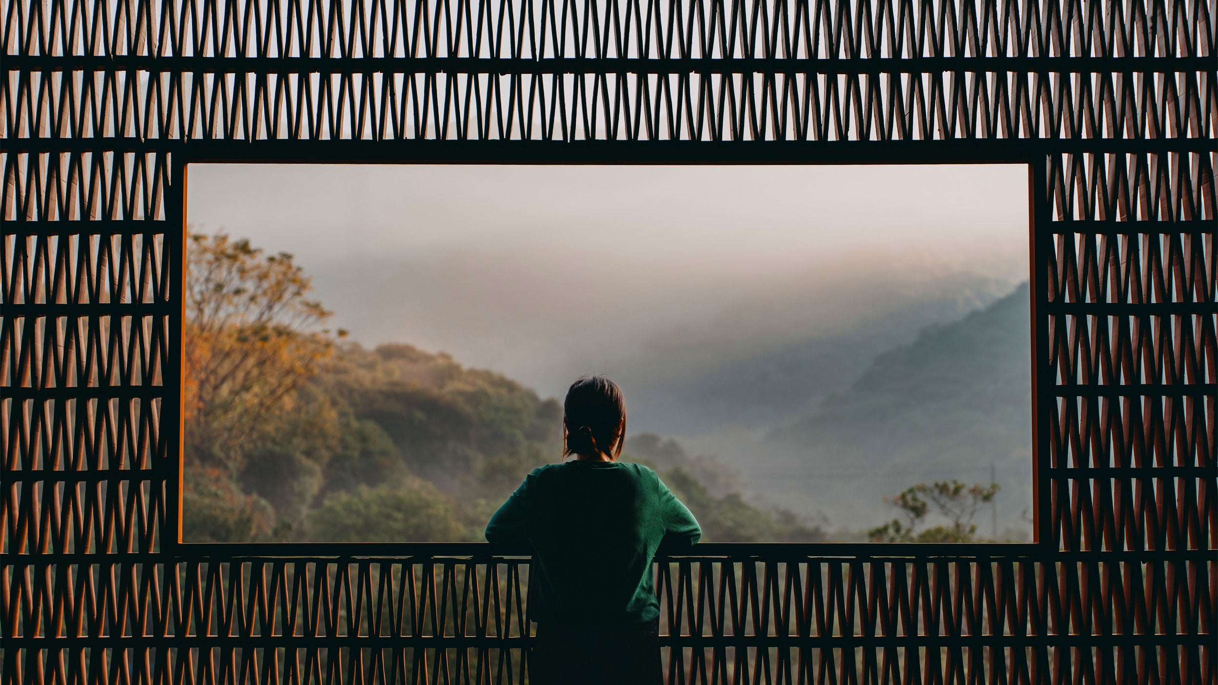 Rear view of young Asian woman enjoying the spectacular scenery during sunrise from a Chinese style balcony with traditional pattern and looking into the distance. Travel and vacation. Exploration and discovery concept