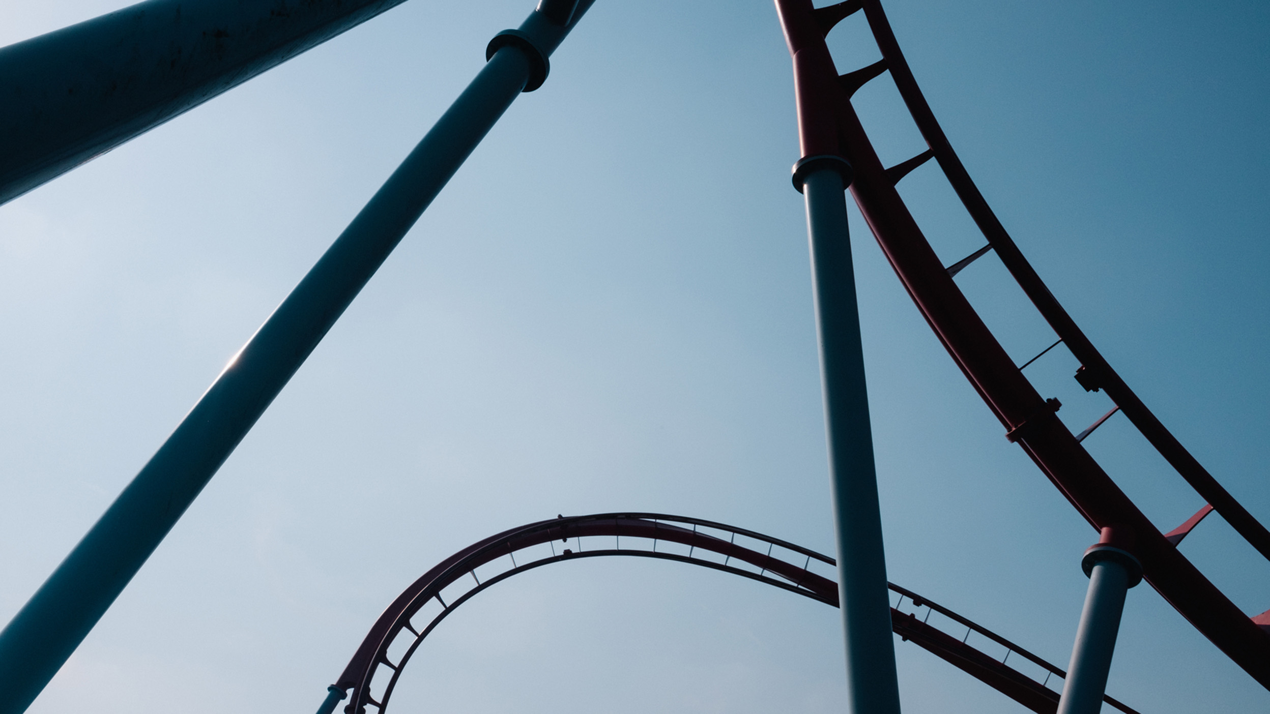 Curving roller coaster tracks against a clear blue sky, symbolising market volatility and changing investment conditions.