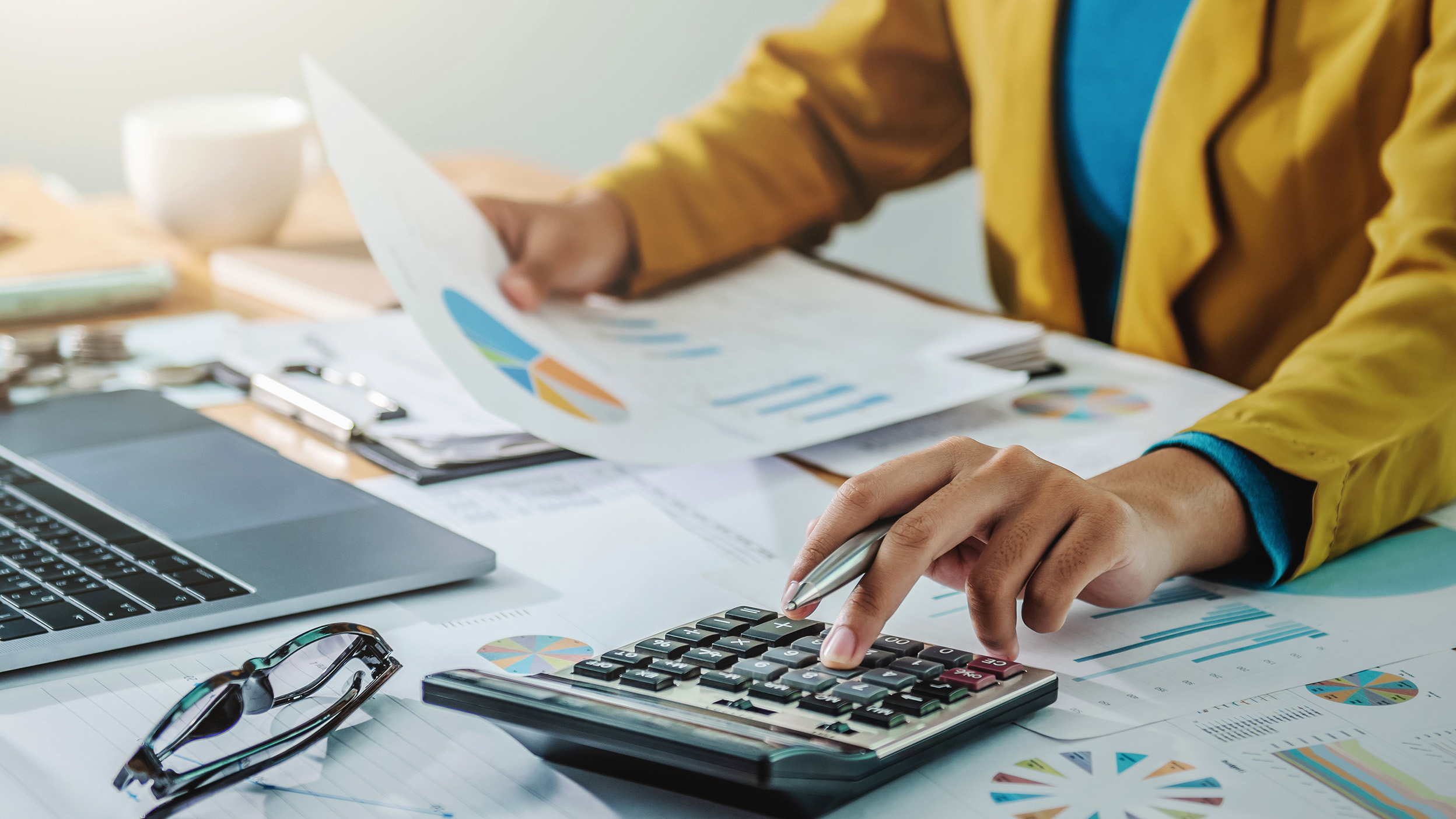 Person reviewing financial reports and charts using a calculator.