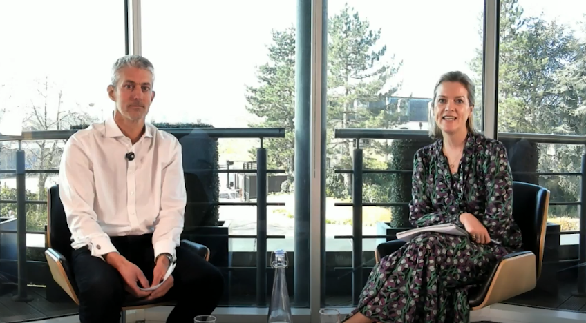 Two individuals sitting in chairs, actively talking to each other, with friendly gestures and focused expressions.