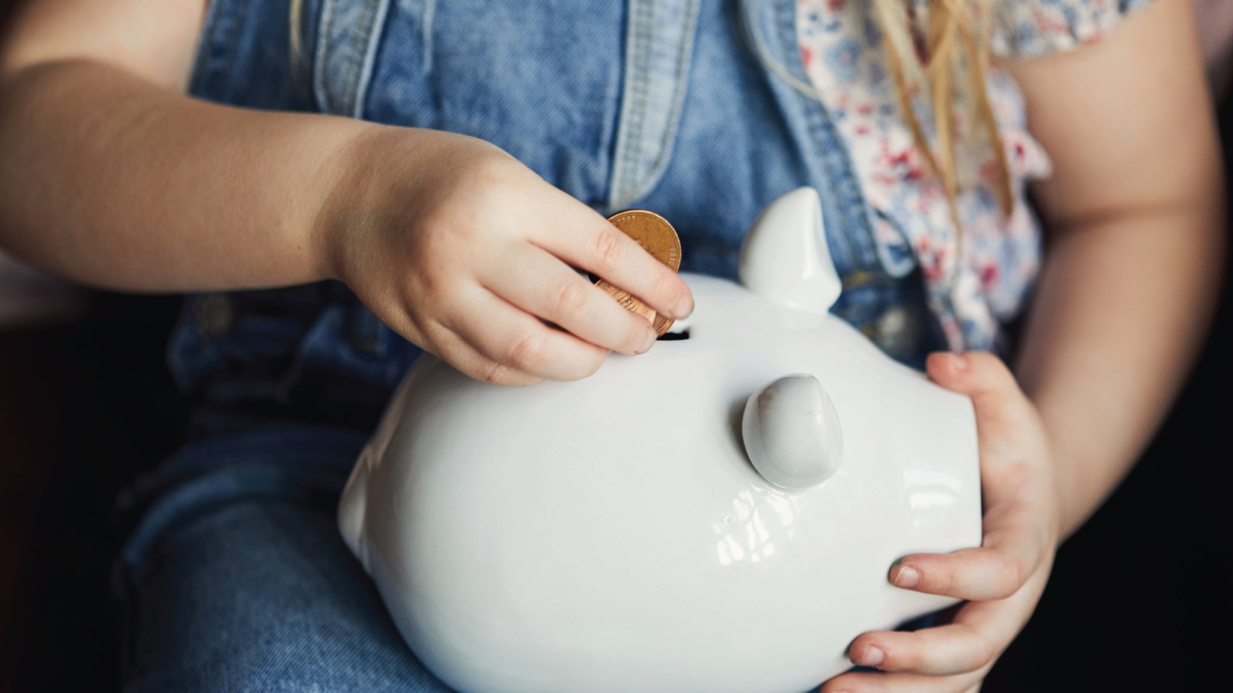 A person placing coins into a pink piggy bank, symbolizing saving money or financial planning. 
