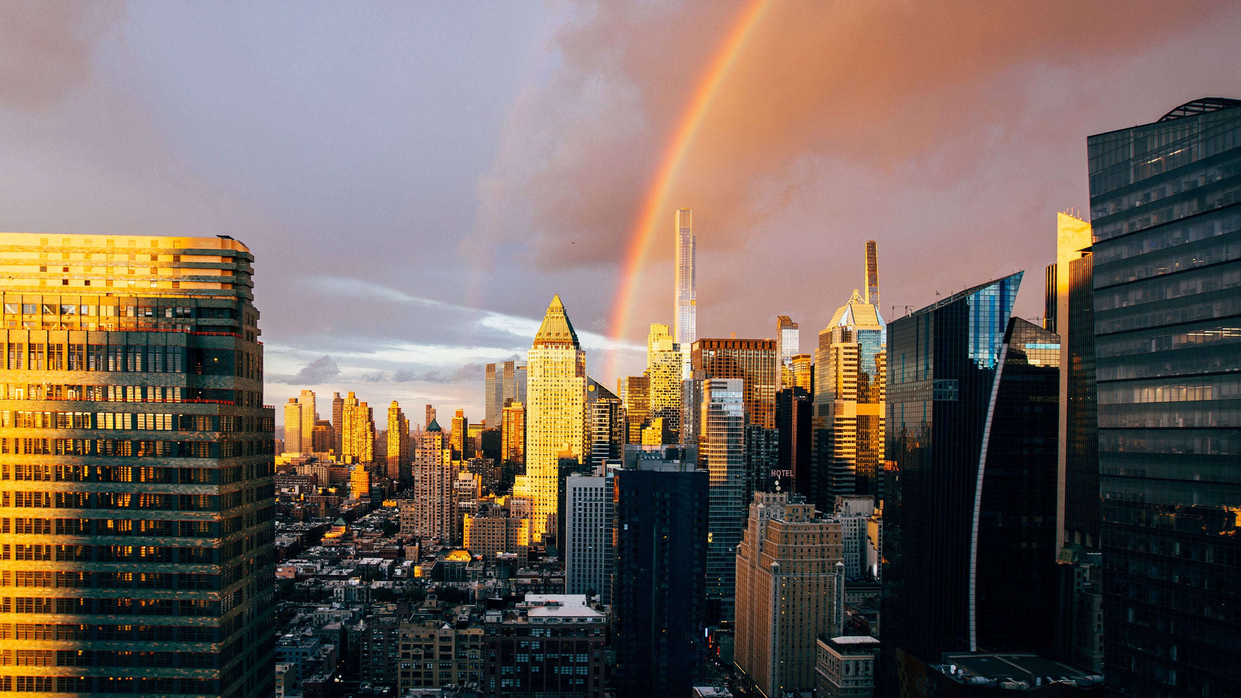 Rainbow over city skyline at sunset.