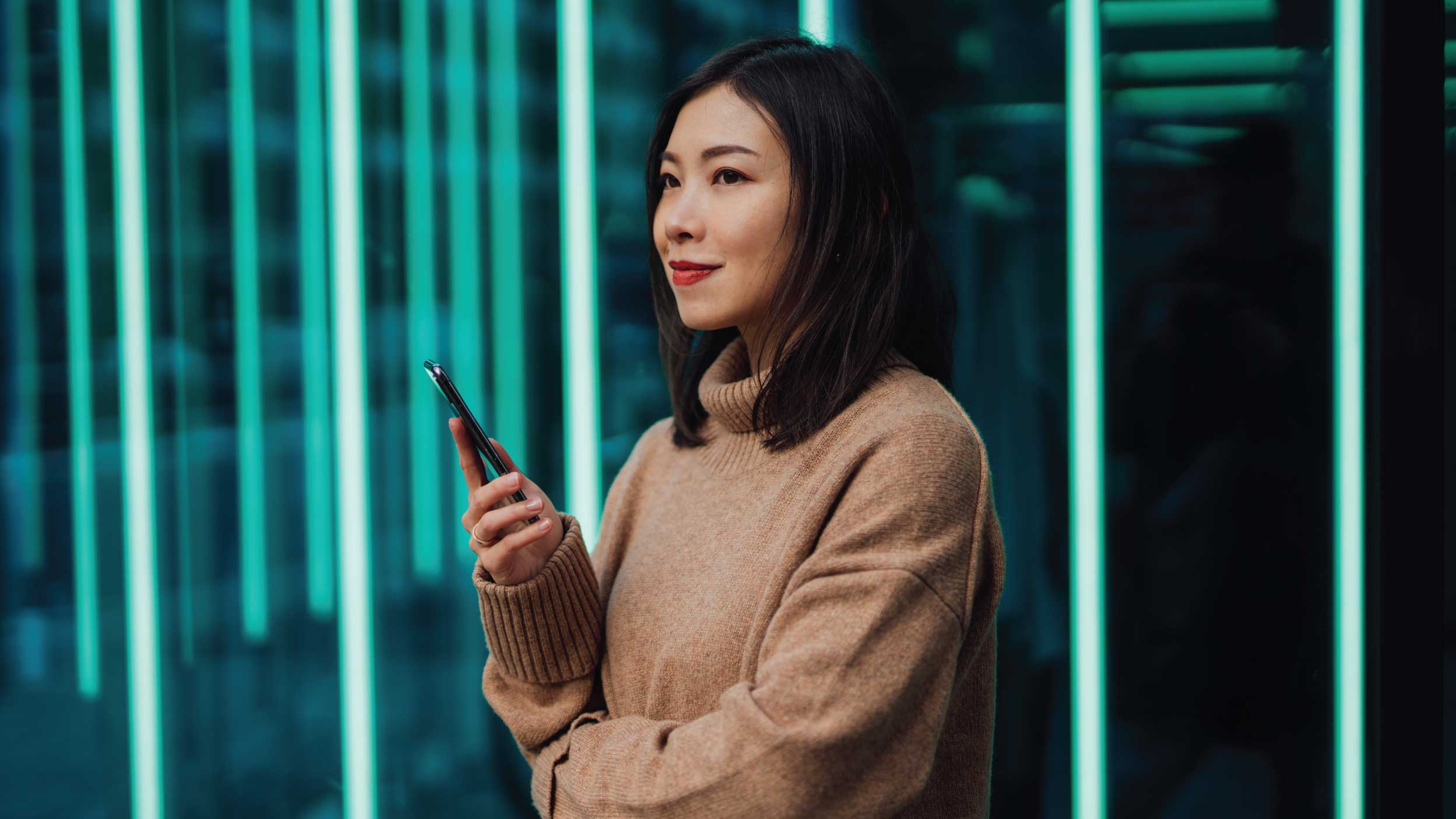 Young woman using mobile phone against futuristic holographic background. New ways of investing - using mobile app to buy stock and cryptocurrency.