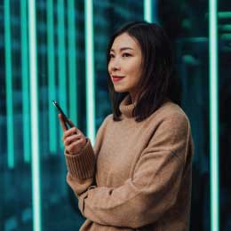 Young%20woman%20using%20mobile%20phone%20against%20futuristic%20holographic%20background.%20New%20ways%20of%20investing%20-%20using%20mobile%20app%20to%20buy%20stock%20and%20cryptocurrency.