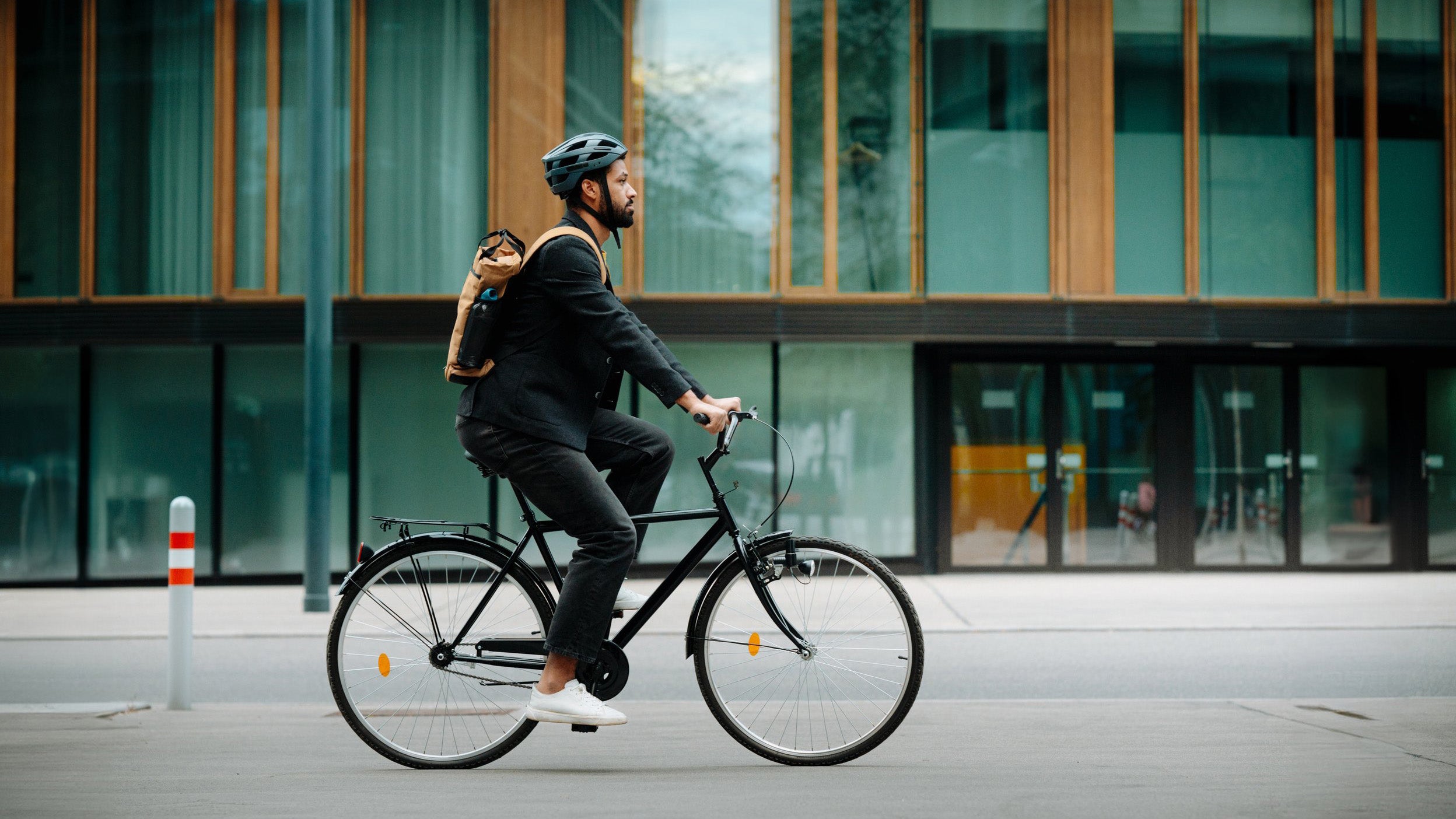 Seitenansicht eines Radfahrers in einer Stadt auf dem Weg zur Arbeit. Junger Geschäftsmann mit Rucksack und Helm, der auf einem Fahrrad von der Arbeit nach Hause fährt.