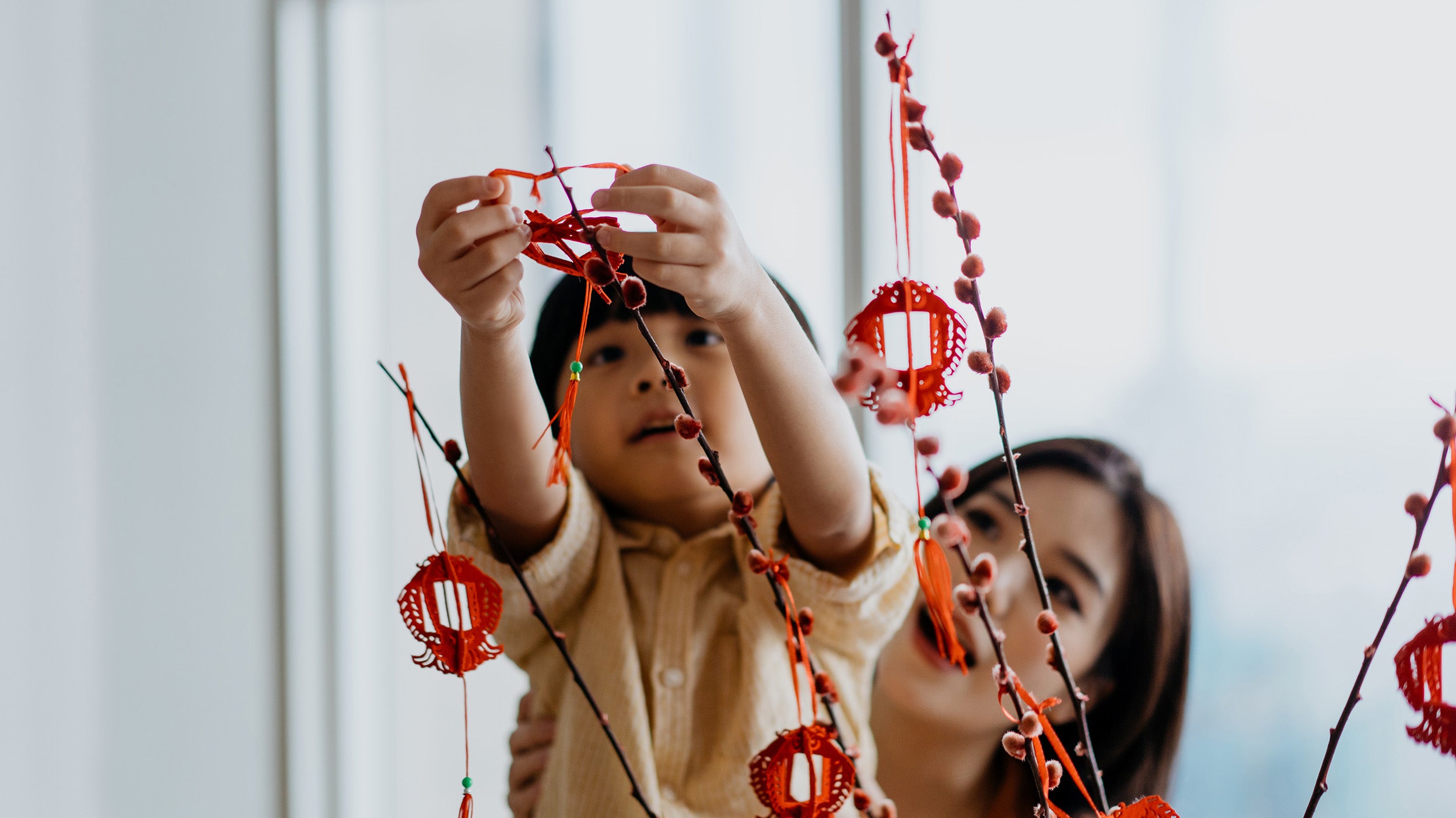 Image of an Asian young chinese boy helping mother to hang Chinese New Year decoration on a plant