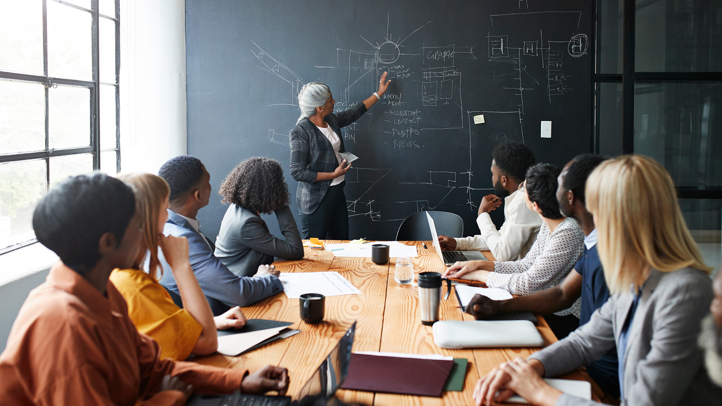 Businesswoman explaining strategy to male and female coworkers sitting in board meeting at workplace.