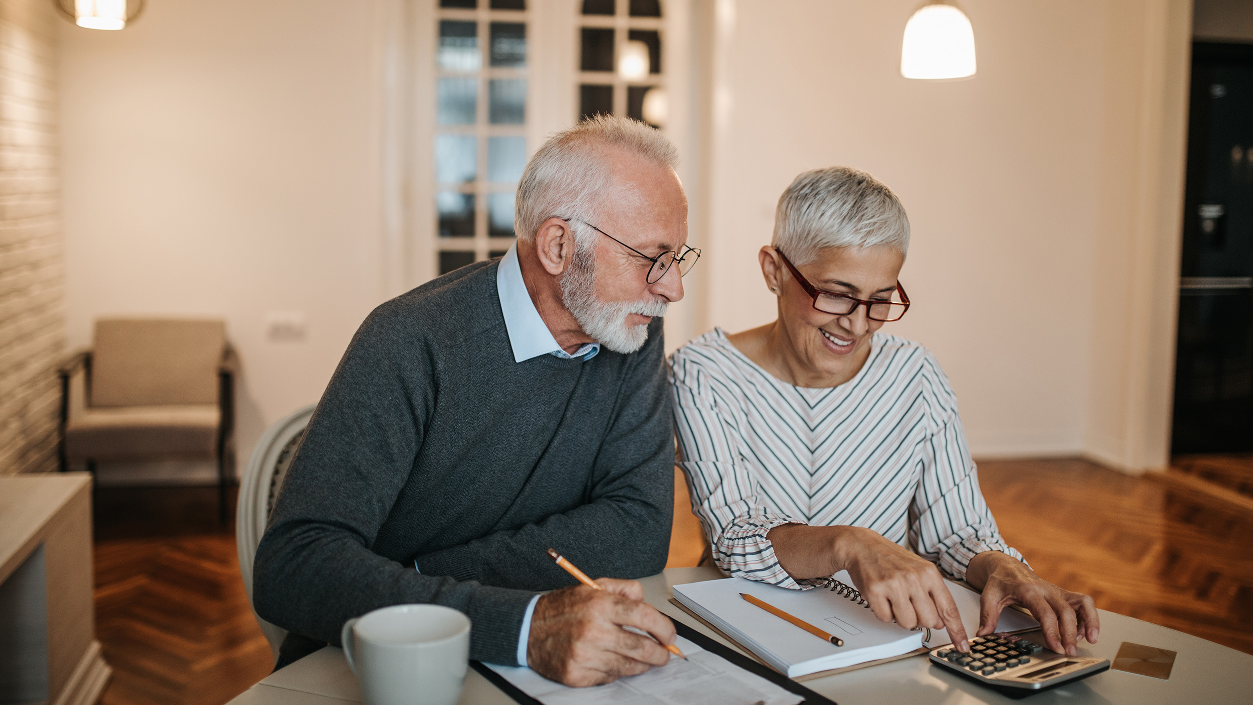 A happy senior couple calculating their finances in a beautiful home.