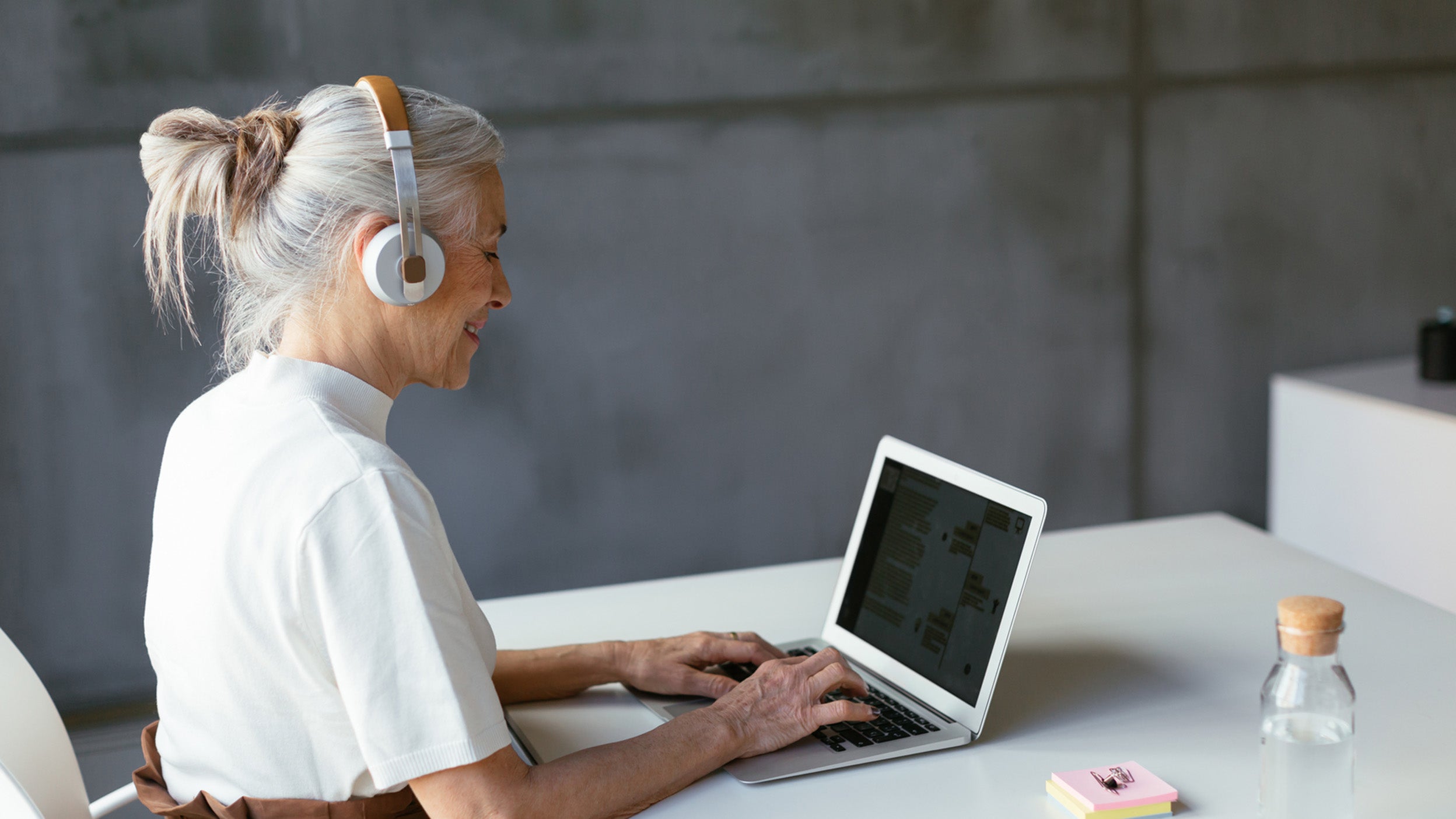 A woman with headphones sits at a desk, focused on her laptop while working