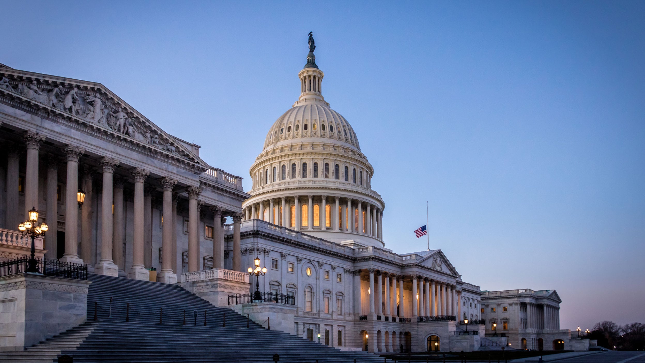 US Capitol building at dusk, with its illuminated dome and neoclassical architecture against a clear evening sky.