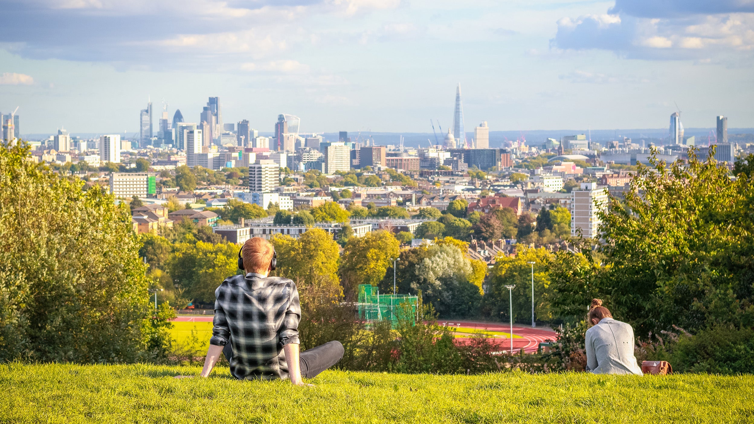 Back view of tourists looking over London city skyline from Parliament Hill in Hampstead Heath