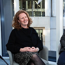 Two%20people%20seated%20indoors%20near%20large%20windows%20with%20city%20buildings%20visible%20outside.