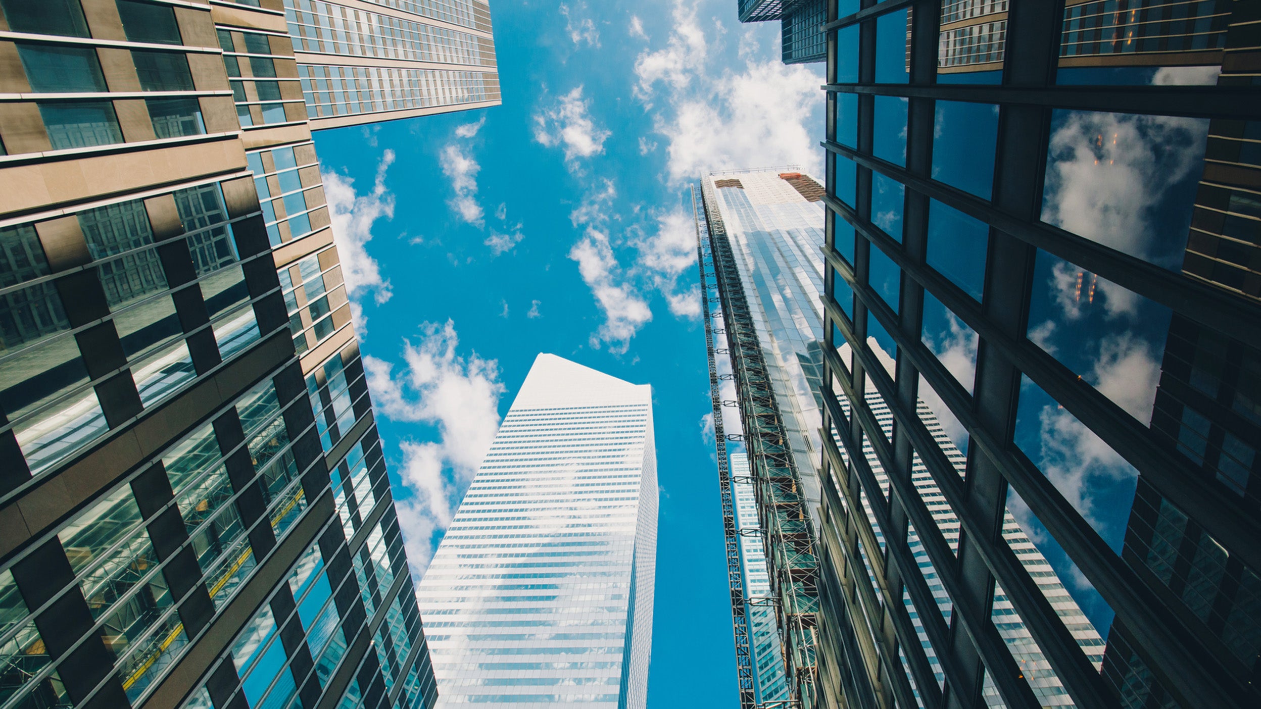 Upward view of modern glass skyscrapers against a bright blue sky with scattered clouds