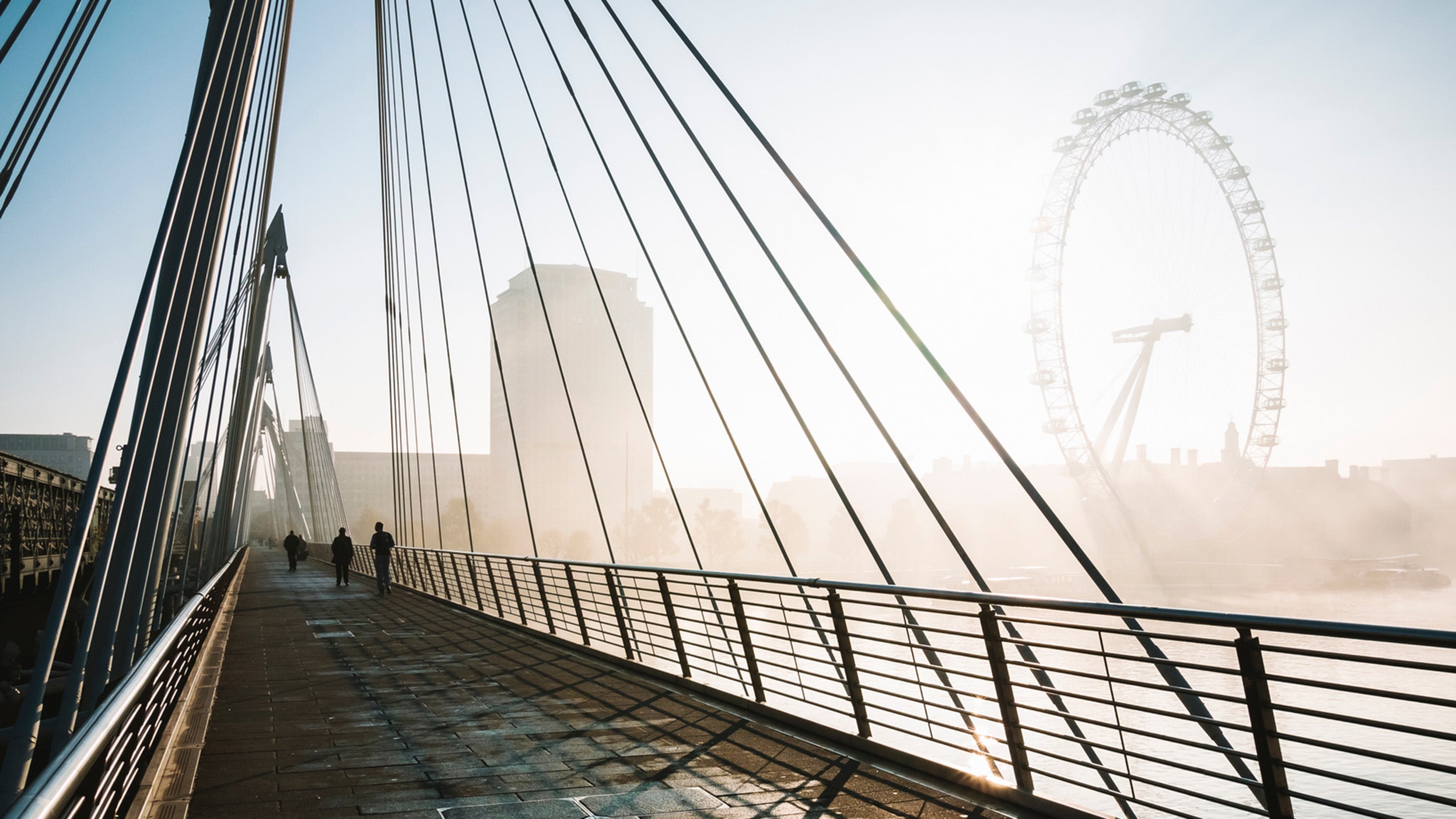 Silhouette of people walking going to work on a contemporary bridge in London in the early morning.