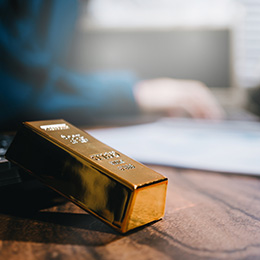 Gold%20bar%20resting%20on%20a%20wooden%20desk%20in%20an%20office%20setting,%20with%20documents%20and%20a%20laptop%20blurred%20in%20the%20background.