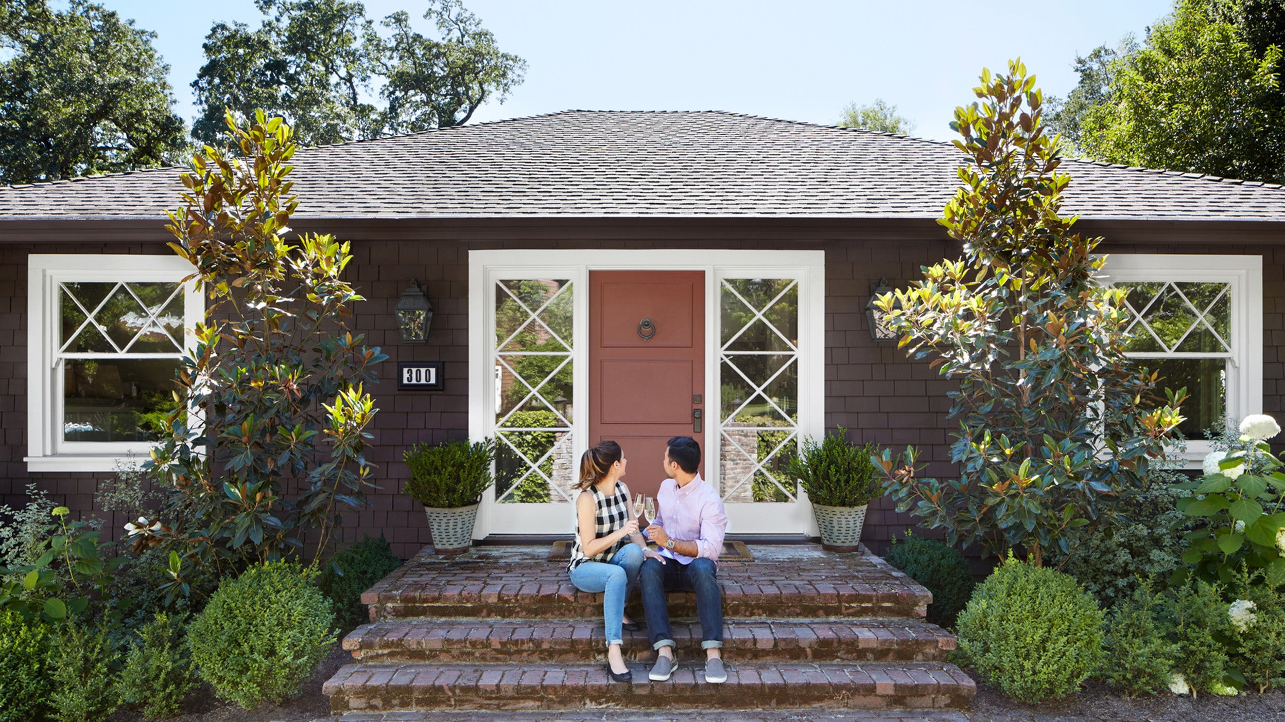 Couple on the front steps of the home they purchased together celebrating drinking champagne for their first new home purchase