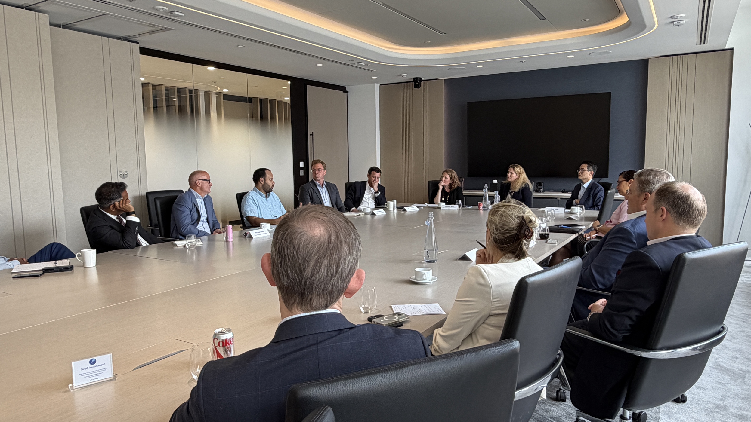 A group of professionals sit around a large conference table in a modern meeting room, engaged in a roundtable discussion