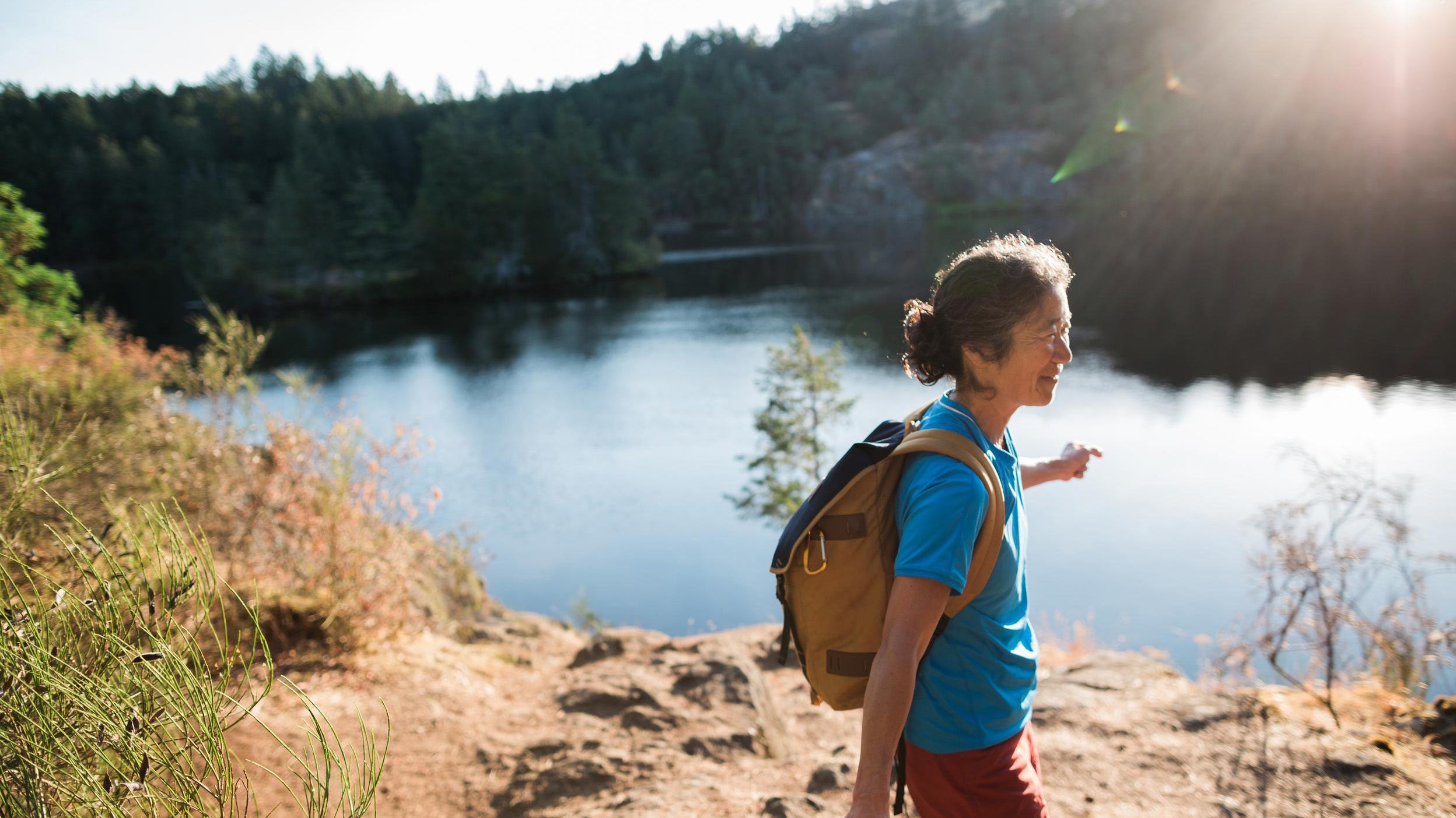 Content mature woman hiking near lake at sunrise