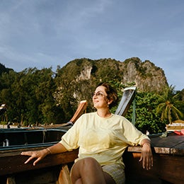 Happy%20beautiful%20woman%20of%20pre-retirement%20age%20in%20sunglasses%20and%20a%20yellow%20T-shirt%20sitting%20on%20board%20a%20wooden%20boat.%20Enjoying%20nature,%20the%20sea,%20the%20Phuket%20islands,%20Krabi%20province.%20