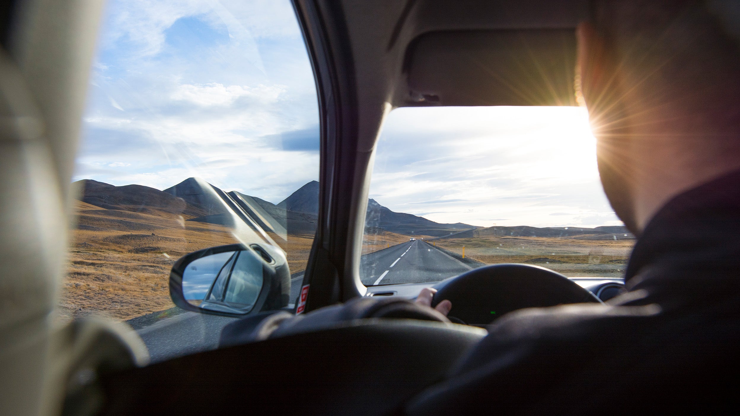 An over the shoulder view of a young man driving the Ring Road as the sun begins to set, in North Iceland.