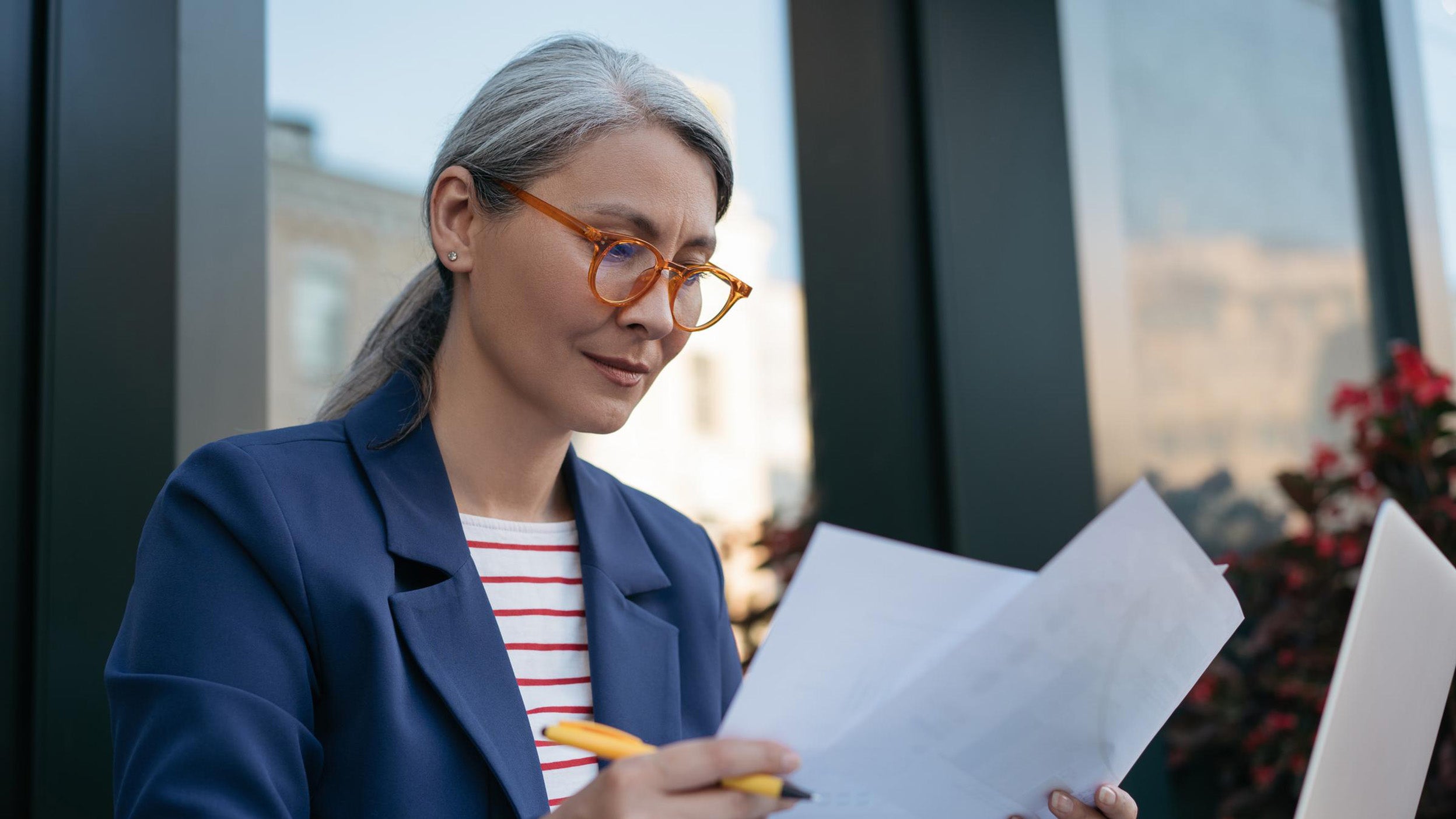 A woman wearing glasses is intently reading a document, focusing on the text in front of her.