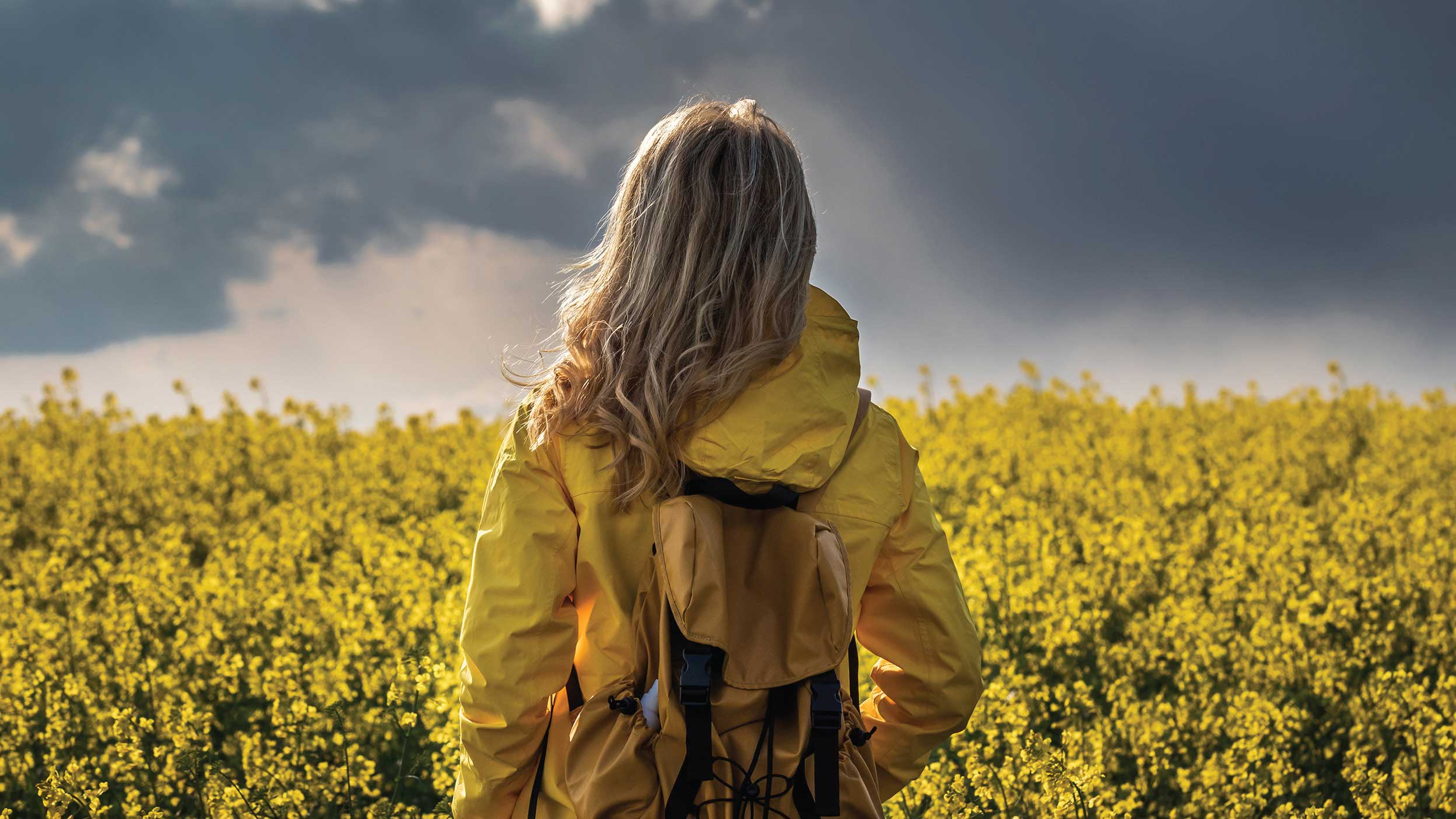 Woman looks out to field with sunlight peaking through rain clouds.