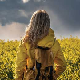 Woman%20looks%20out%20to%20field%20with%20sunlight%20peaking%20through%20rain%20clouds.