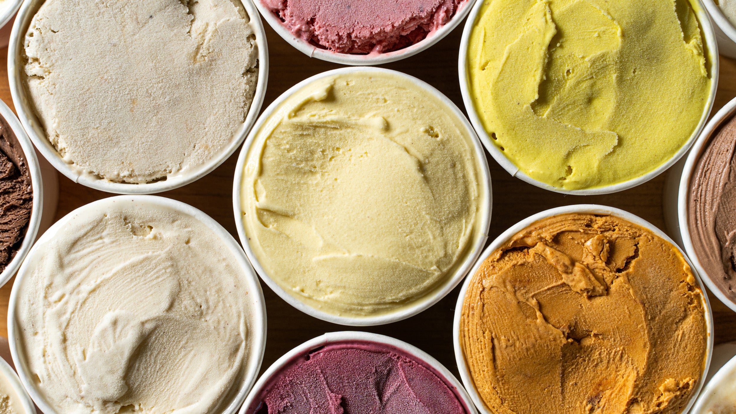 Top-down view of several tubs of ice cream in different colors and flavors arranged closely together.