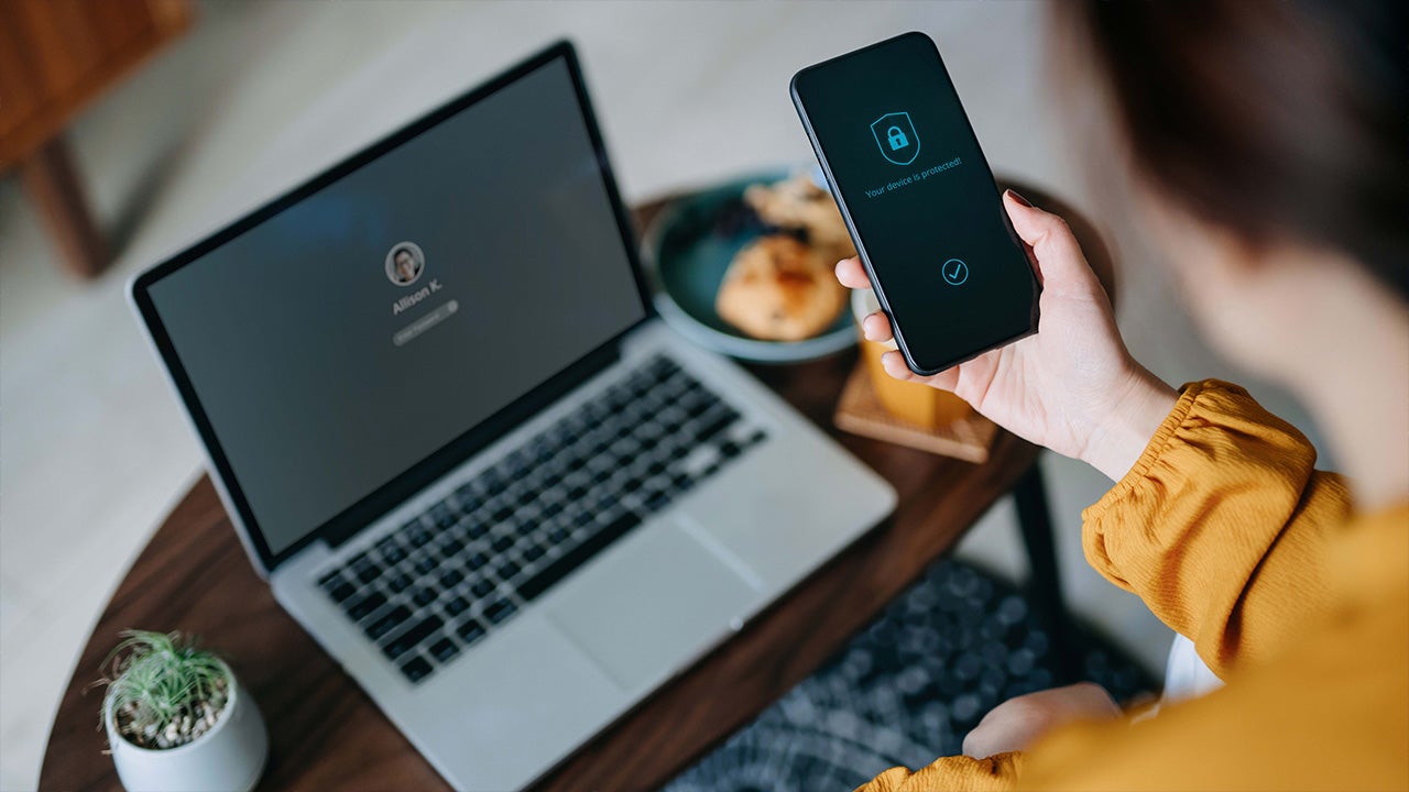  A woman looks at their cellphone and their computer while securing their data with two-factor authorization. Technology developed by Invesco QQQ ETF holding companies provides exposure to the data privacy sector. 