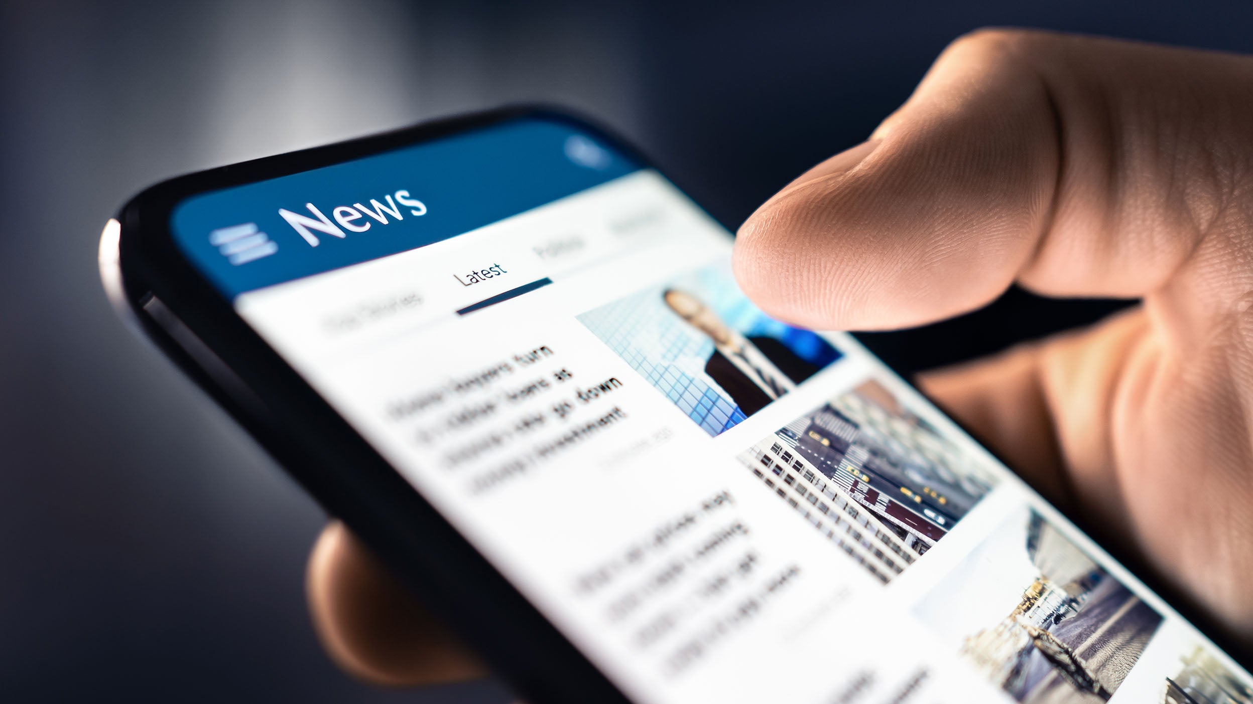 Close-up shot of a hand holding a phone with a news article on it.