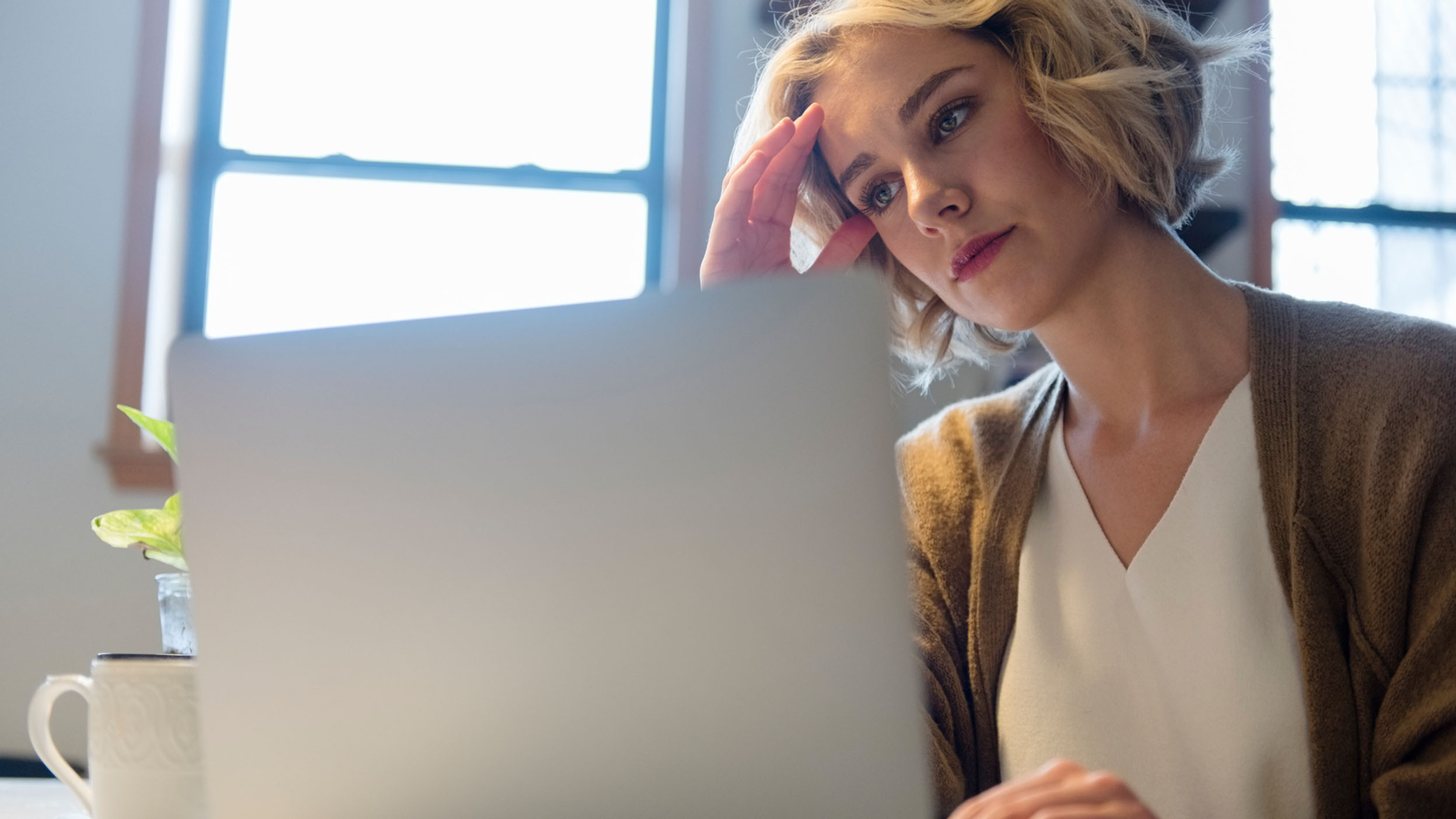 A woman looks at her laptop with a look of concern on her face.