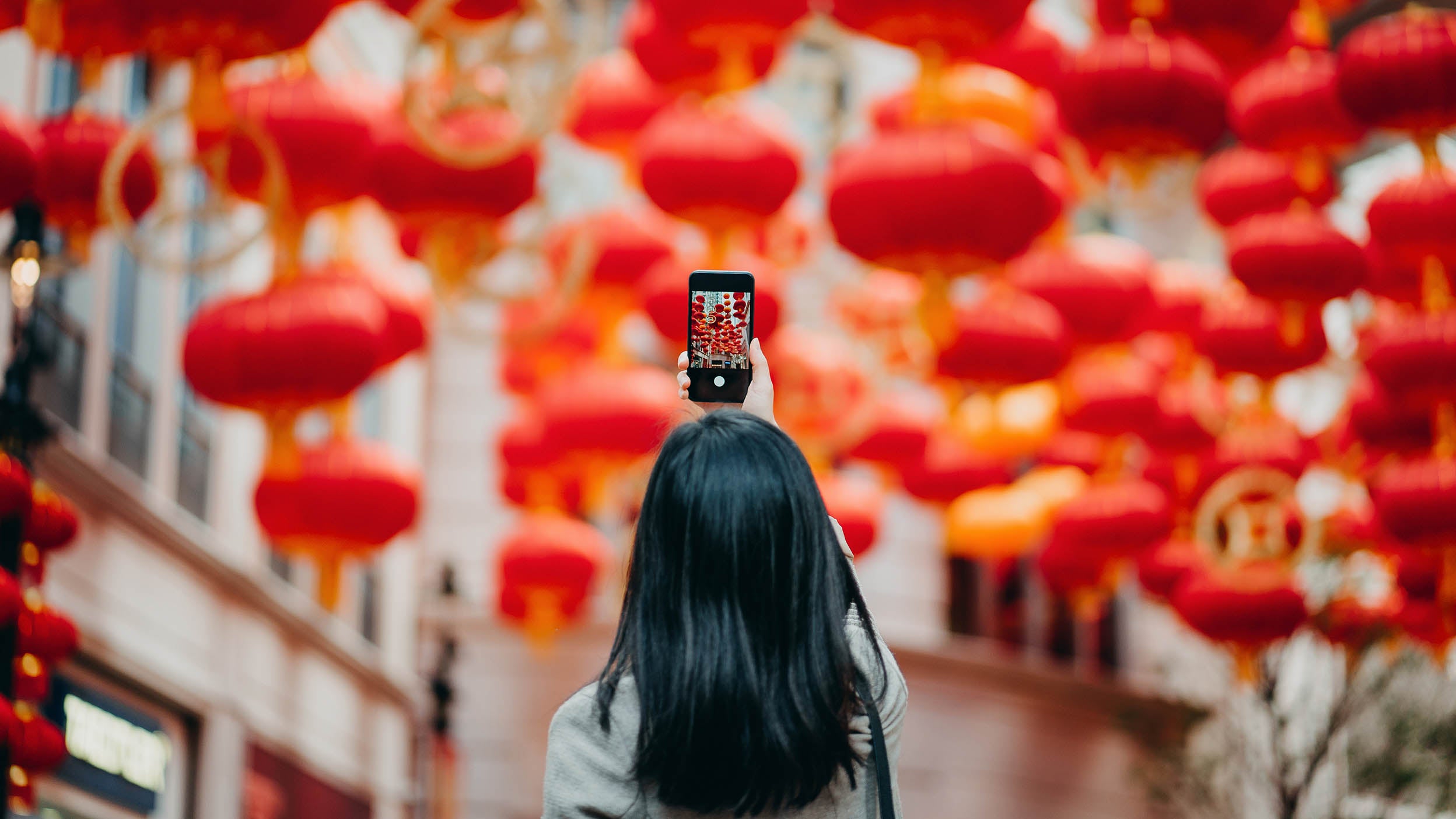 Vue arrière d’une femme prenant des photos de lanternes rouges chinoises traditionnelles avec téléphone intelligent sur la rue.