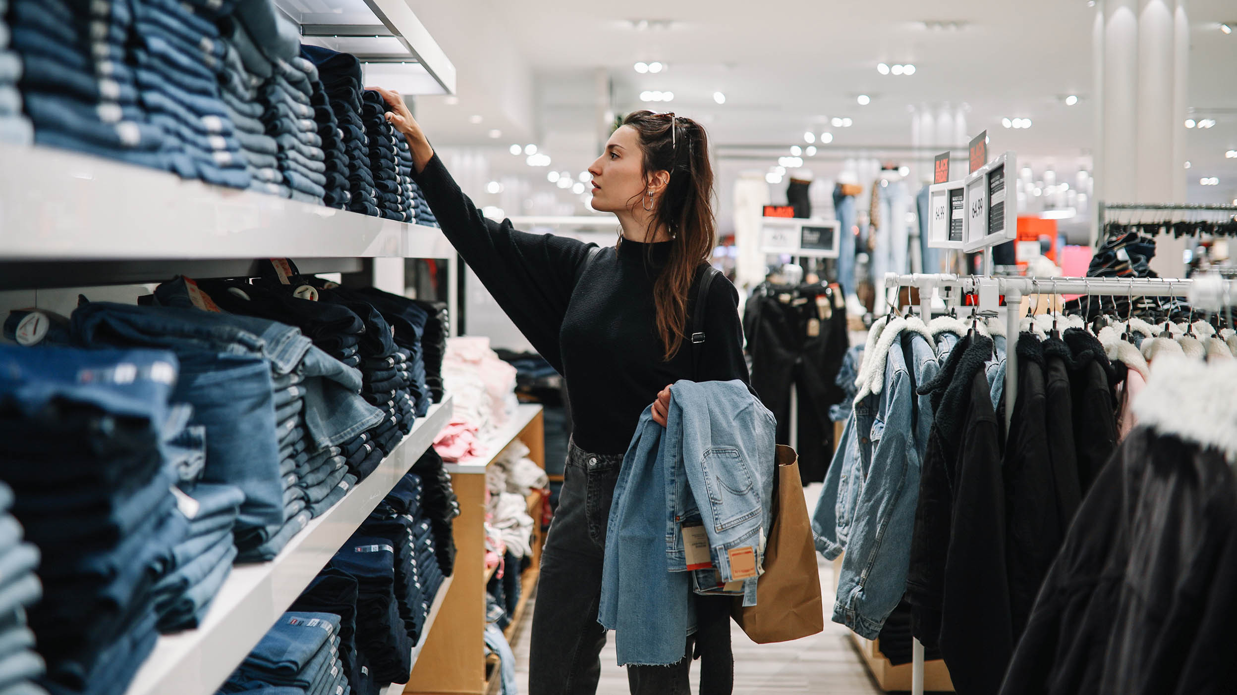 Woman in mid 30s goes shopping for denim jeans in a clothing store.