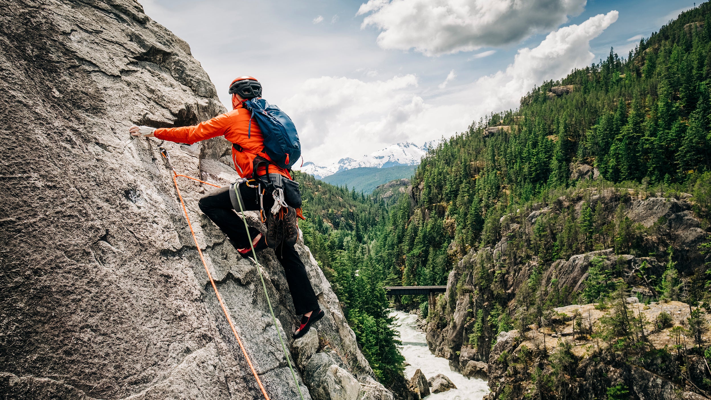 A rock climber leads up a rock face high above a mountain's river valley near Whistler, BC.