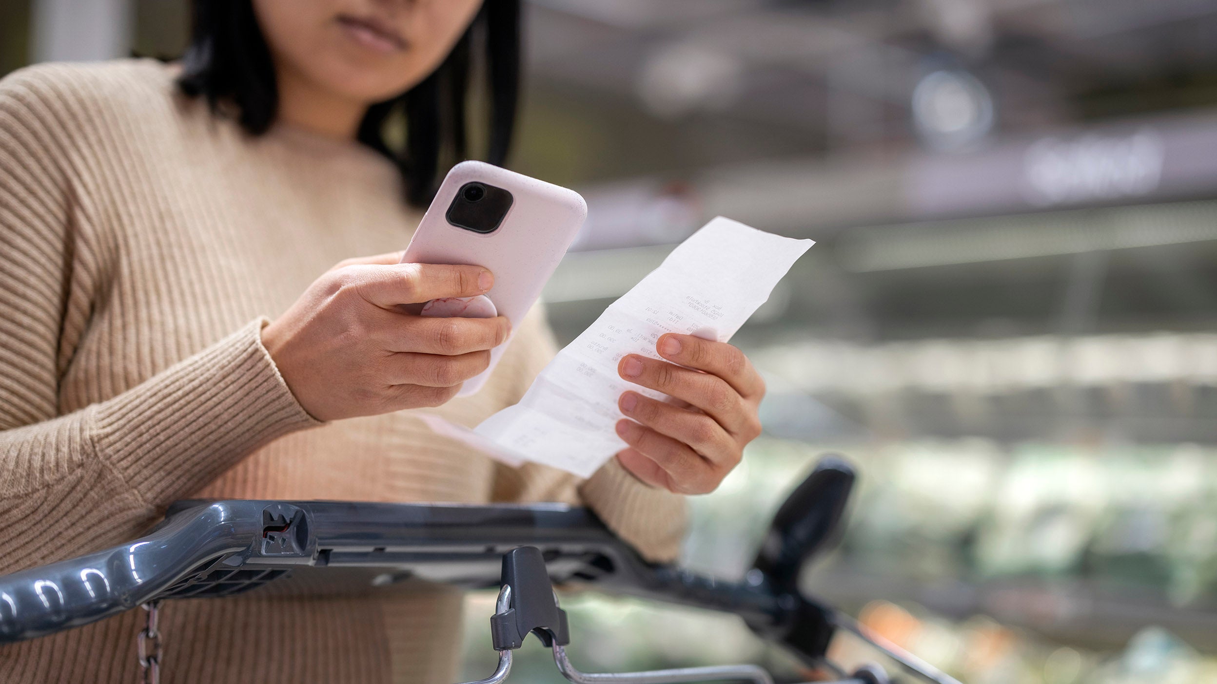 A woman examining a list while using a smartphone at the supermarket