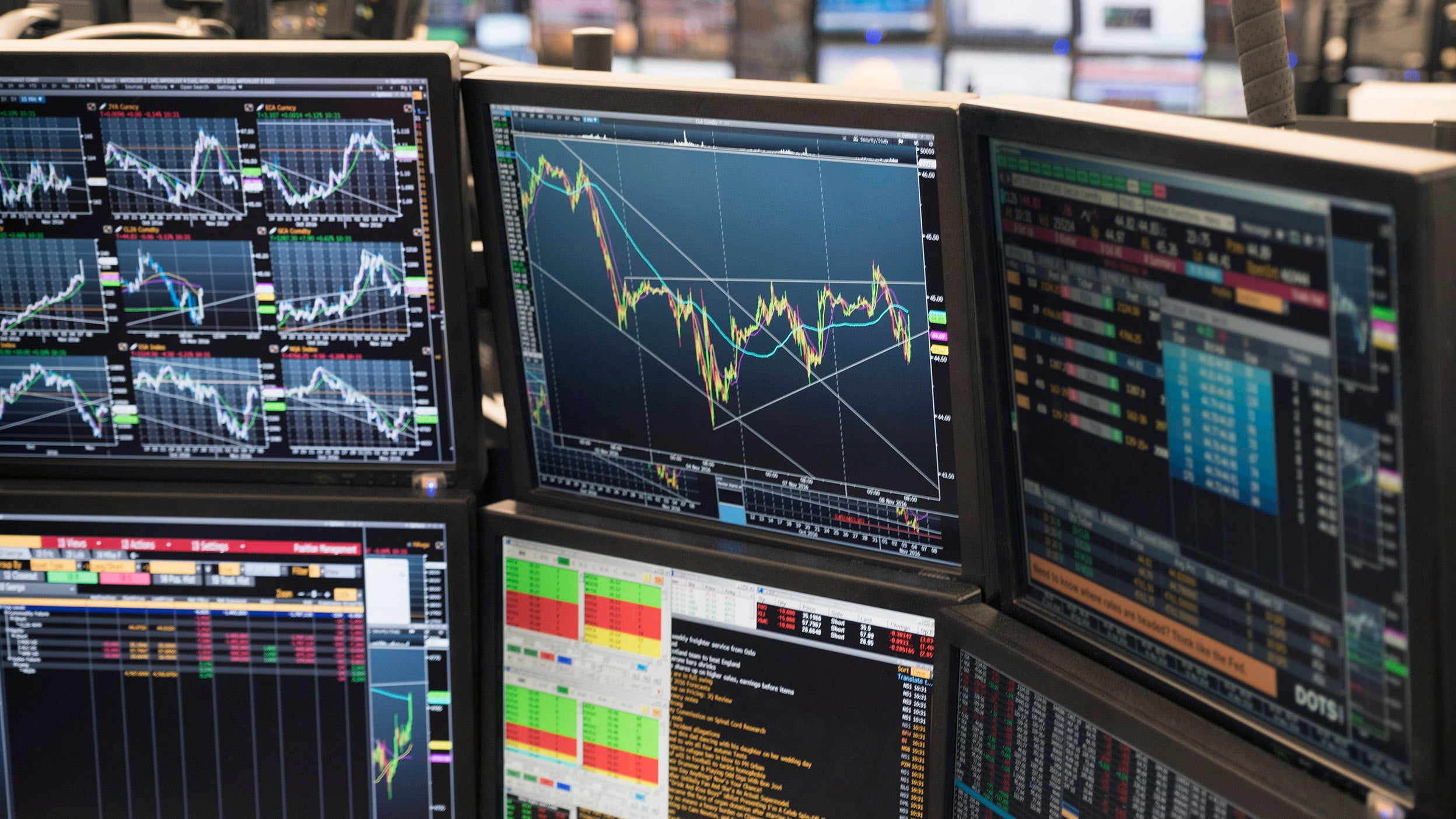 Stock market graphs on multiple computer screens on a trading floor.