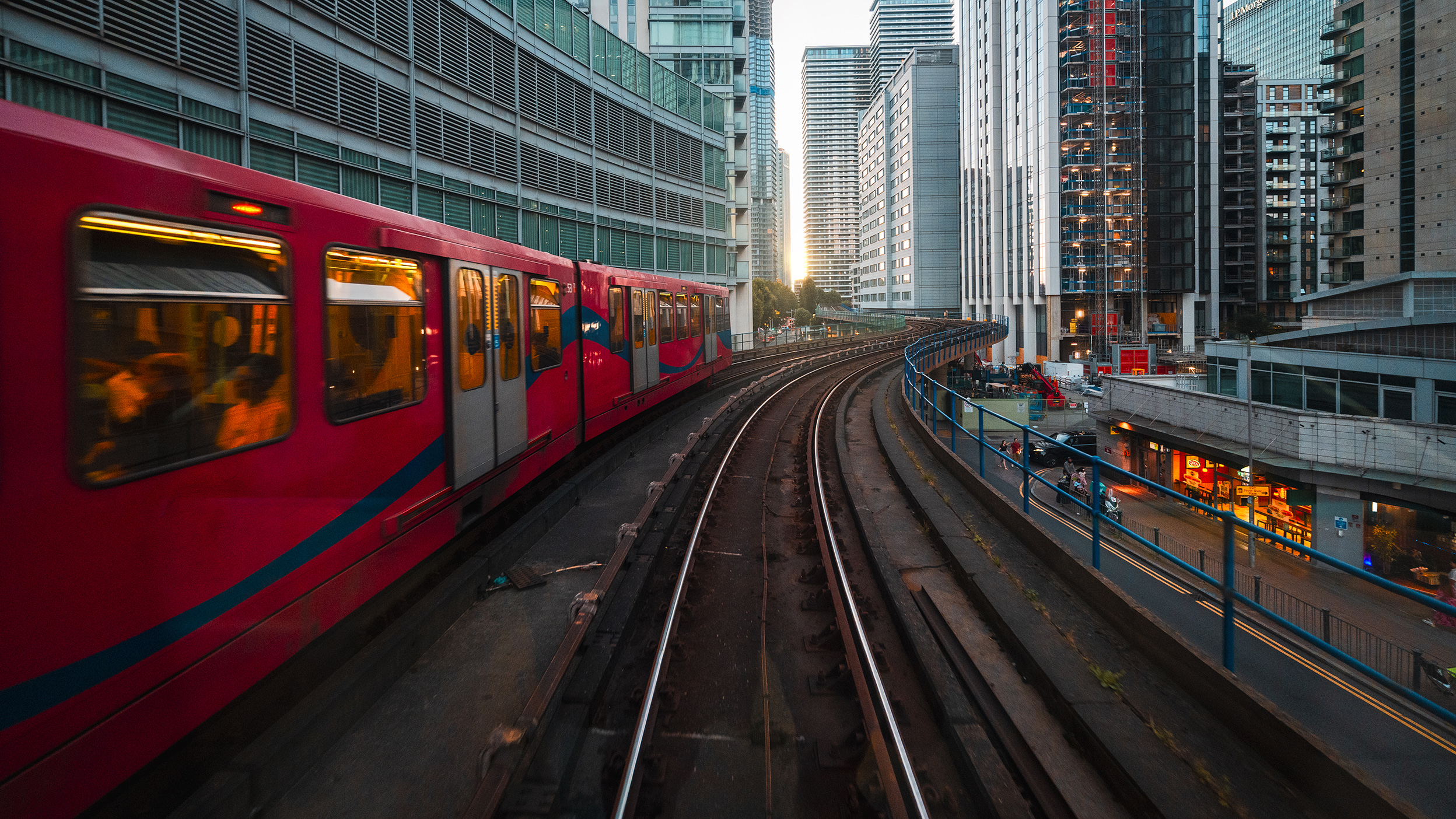 Red commuter train on elevated tracks through a modern city at sunset.